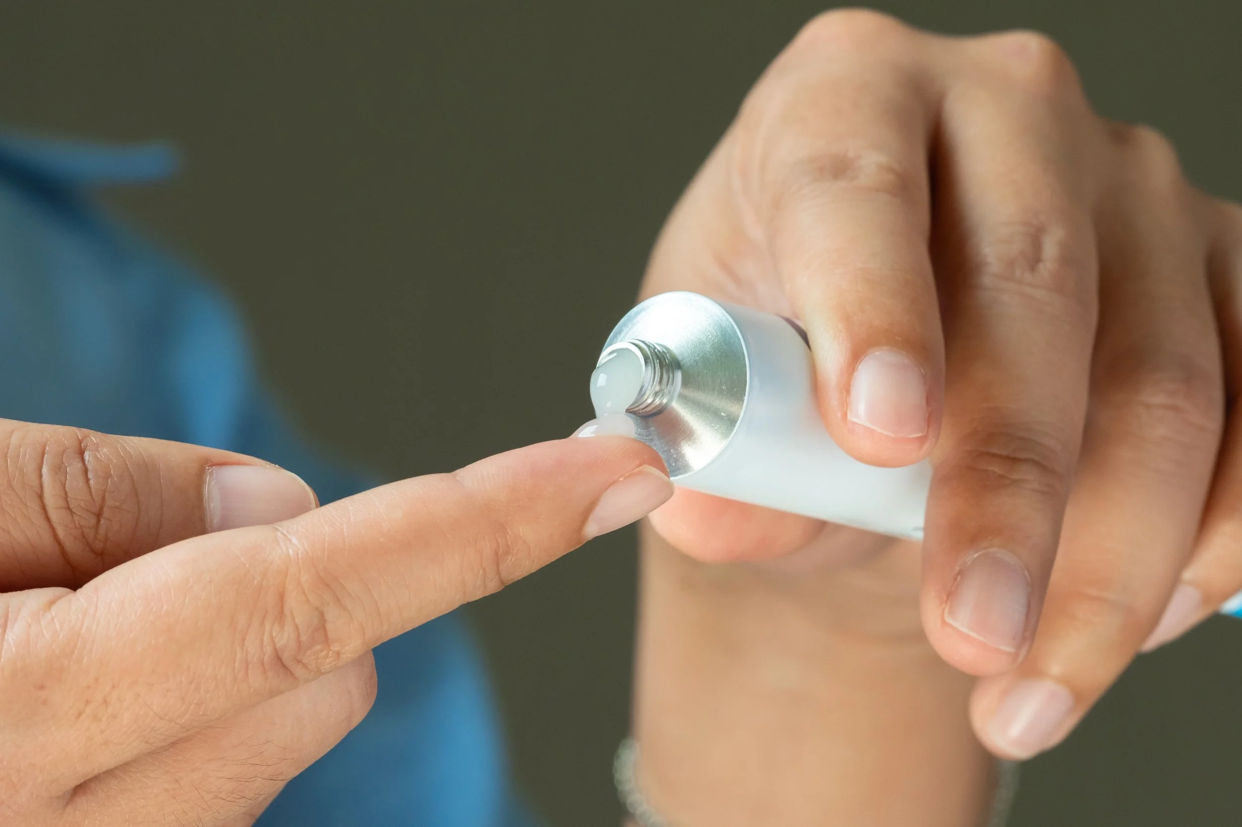 Close-up of a person applying cream or ointment from a squeeze tube onto their finger.