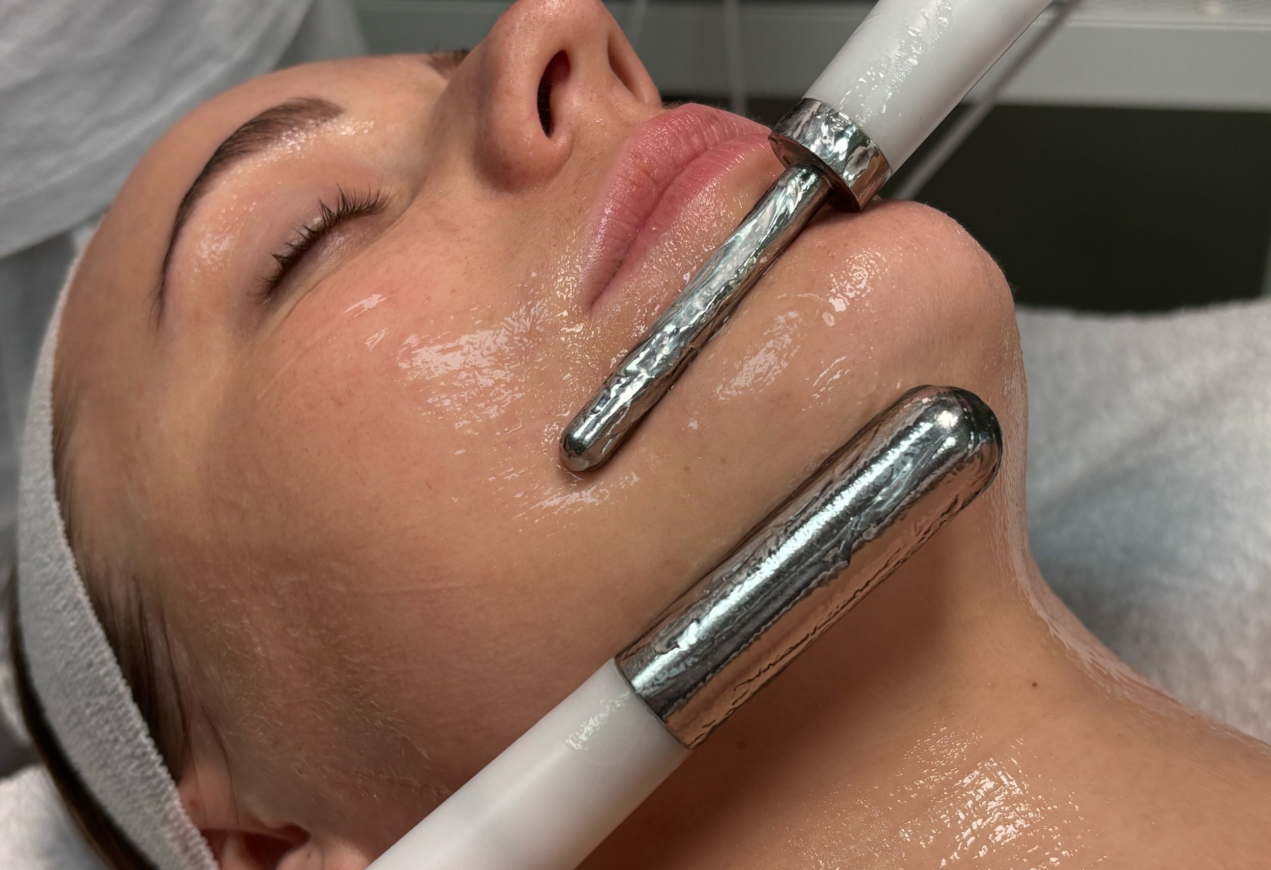 Close-up of a woman receiving a facial treatment with a handheld device on her face in a spa or clinic setting.