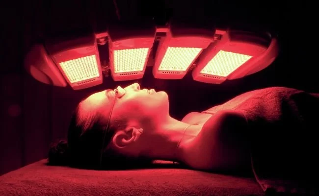 Person lying on a treatment bed undergoing red light therapy with LED panels above.
