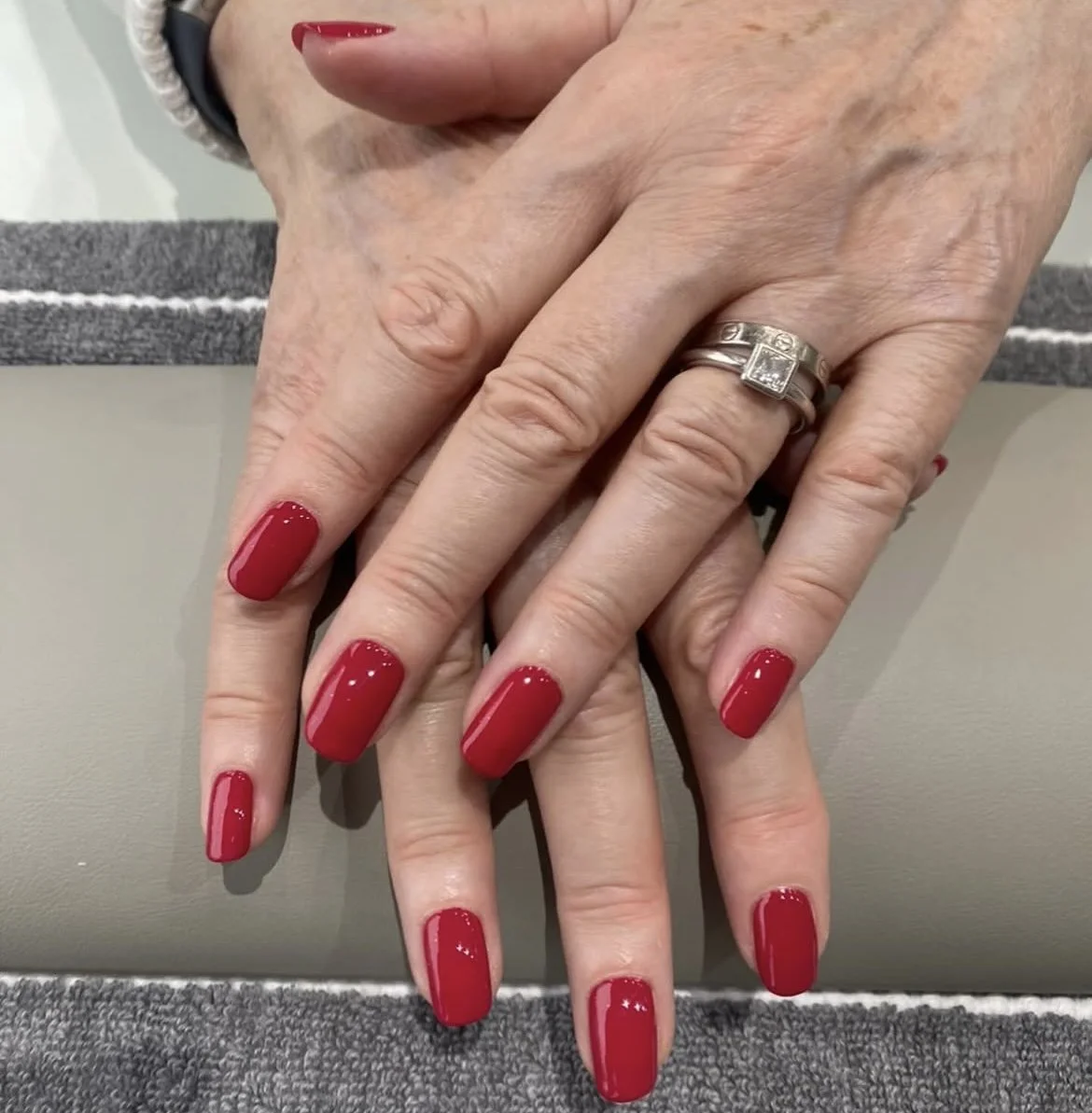 Close-up of a woman's hands with red manicured nails, wearing a silver ring with a square-shaped gemstone.