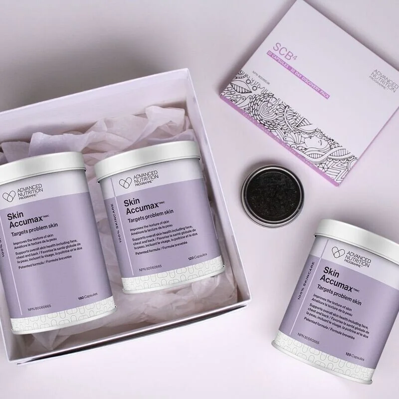 Three bottles of Skin Accumax supplement in a white box, with a black container, a colorful pamphlet, and a small jar nearby on a white surface.