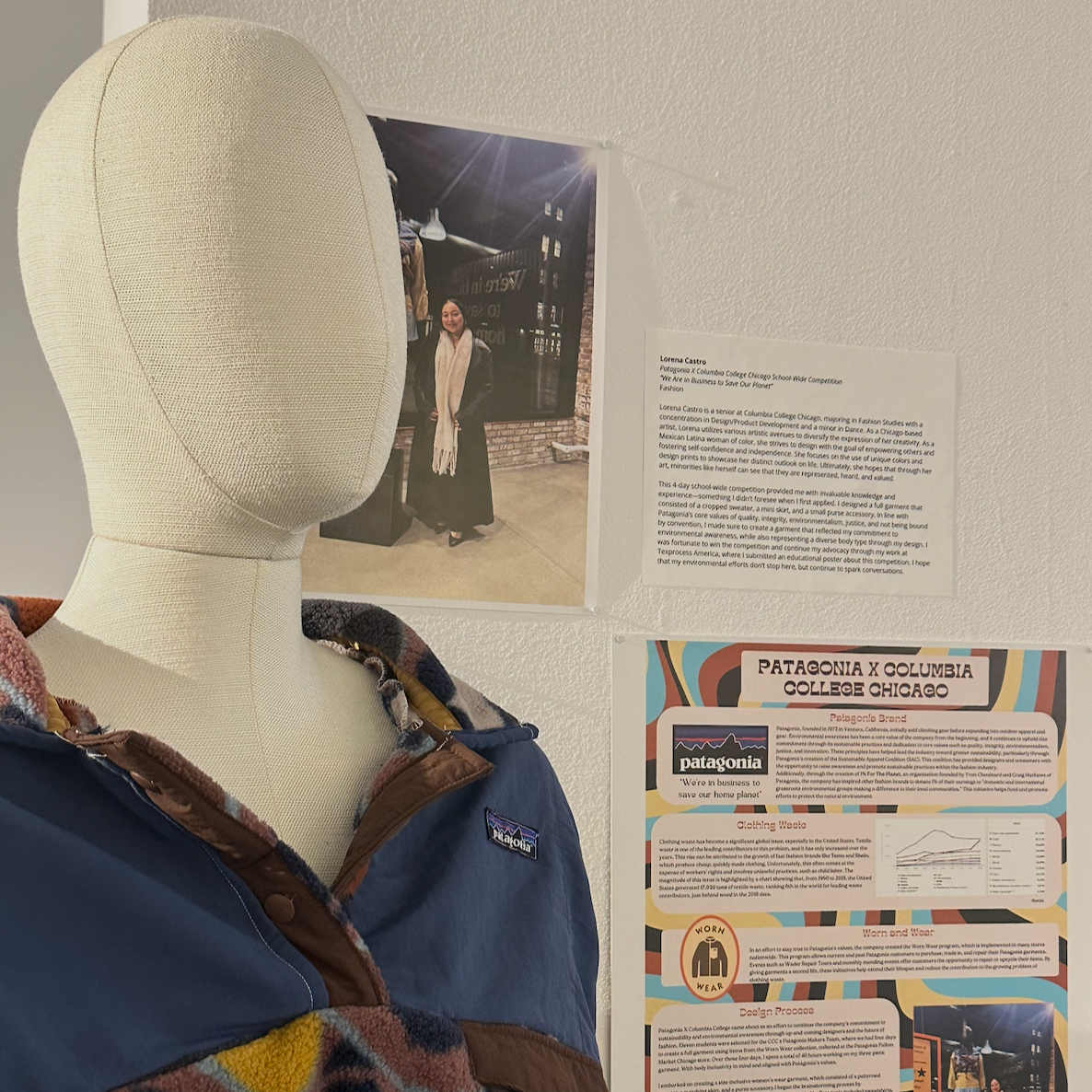 A mannequin wearing a Patagonia jacket with a colorful patterned collar, in front of a wall with photographs and informational posters related to Patagonia and Columbia College Chicago.