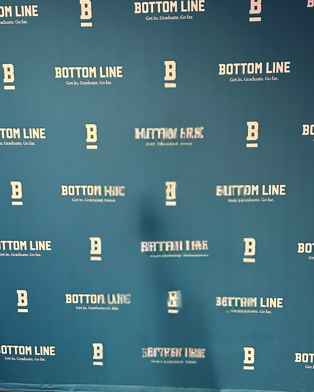 Blue backdrop with repeating white text and logos, displaying phrases like "Bottom Line," "Get in. Graduate. Go far," and students' names such as "Hutton Hayes."
