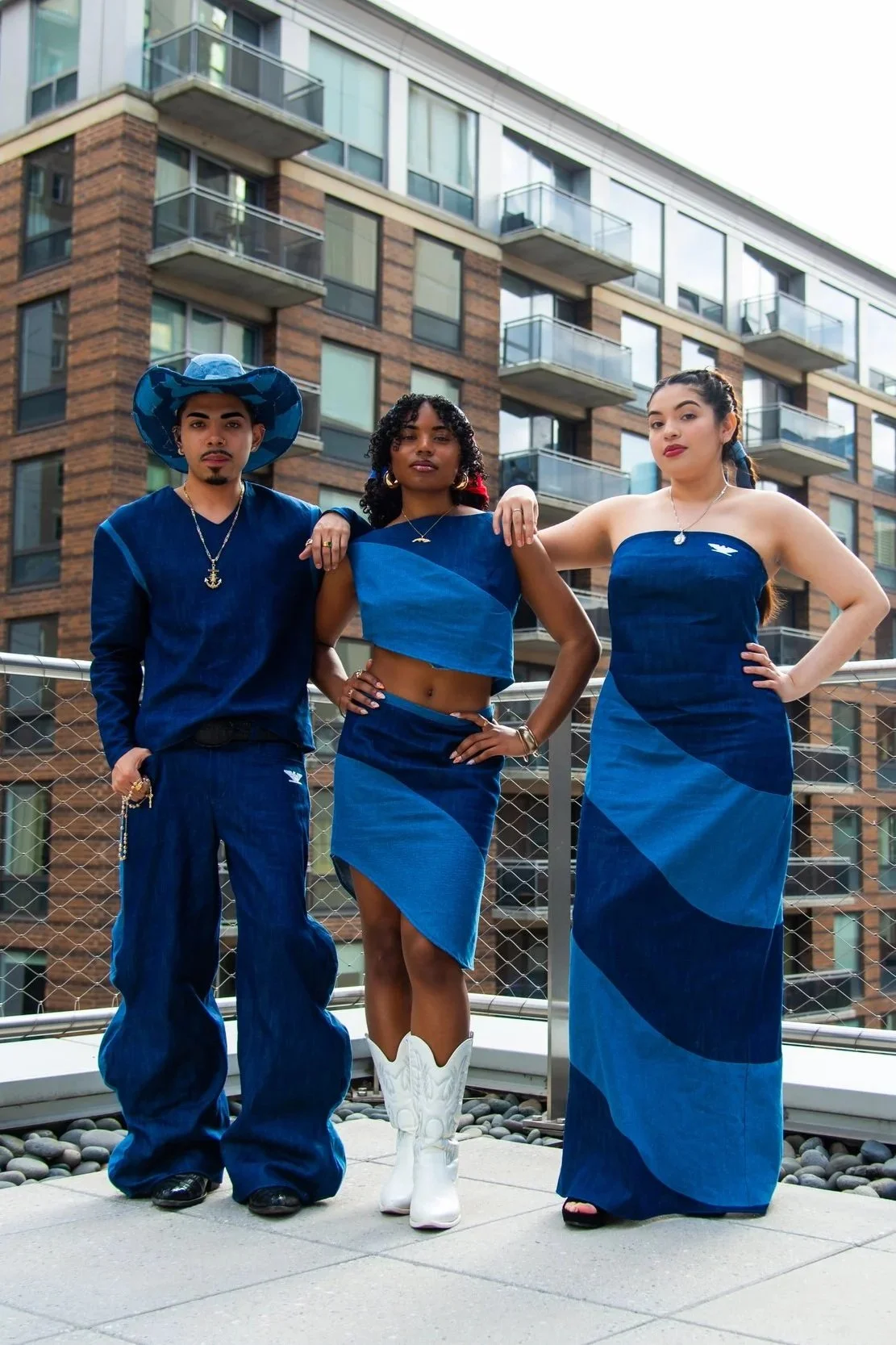 Three young adults posing outdoors in front of a modern apartment building, dressed in coordinated blue outfits with a casual yet fashionable style.