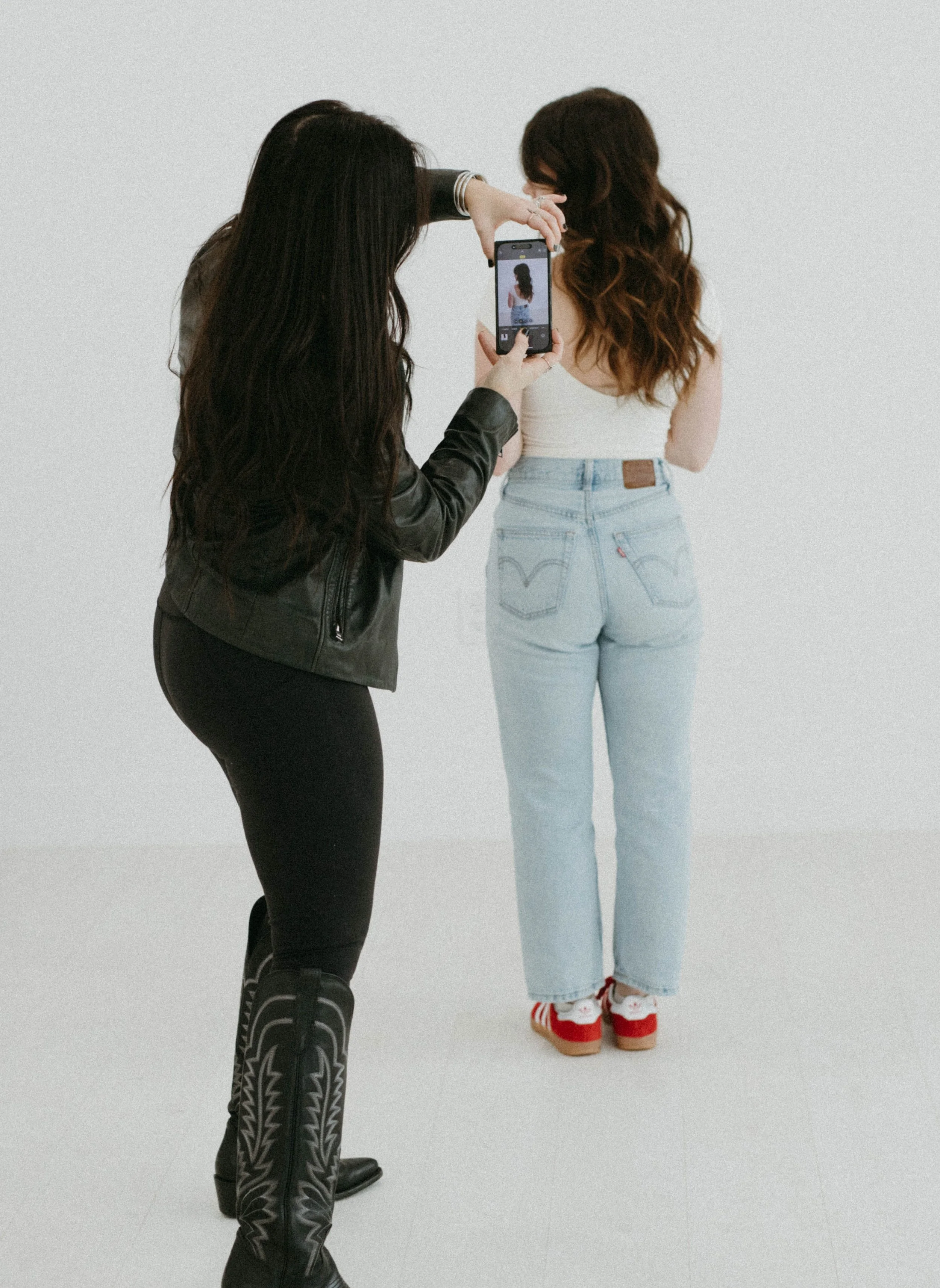 Two women taking a photo of each other in front of a plain white wall.