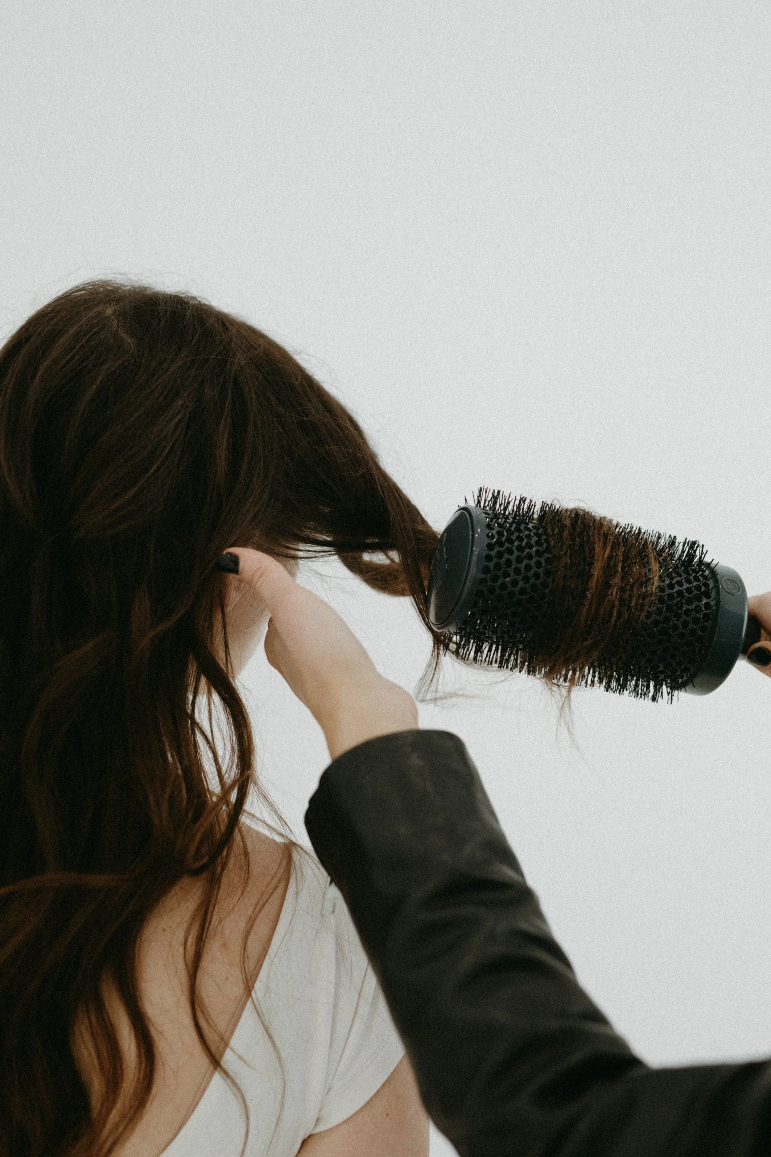 Person using a round hairbrush to style long brown hair.