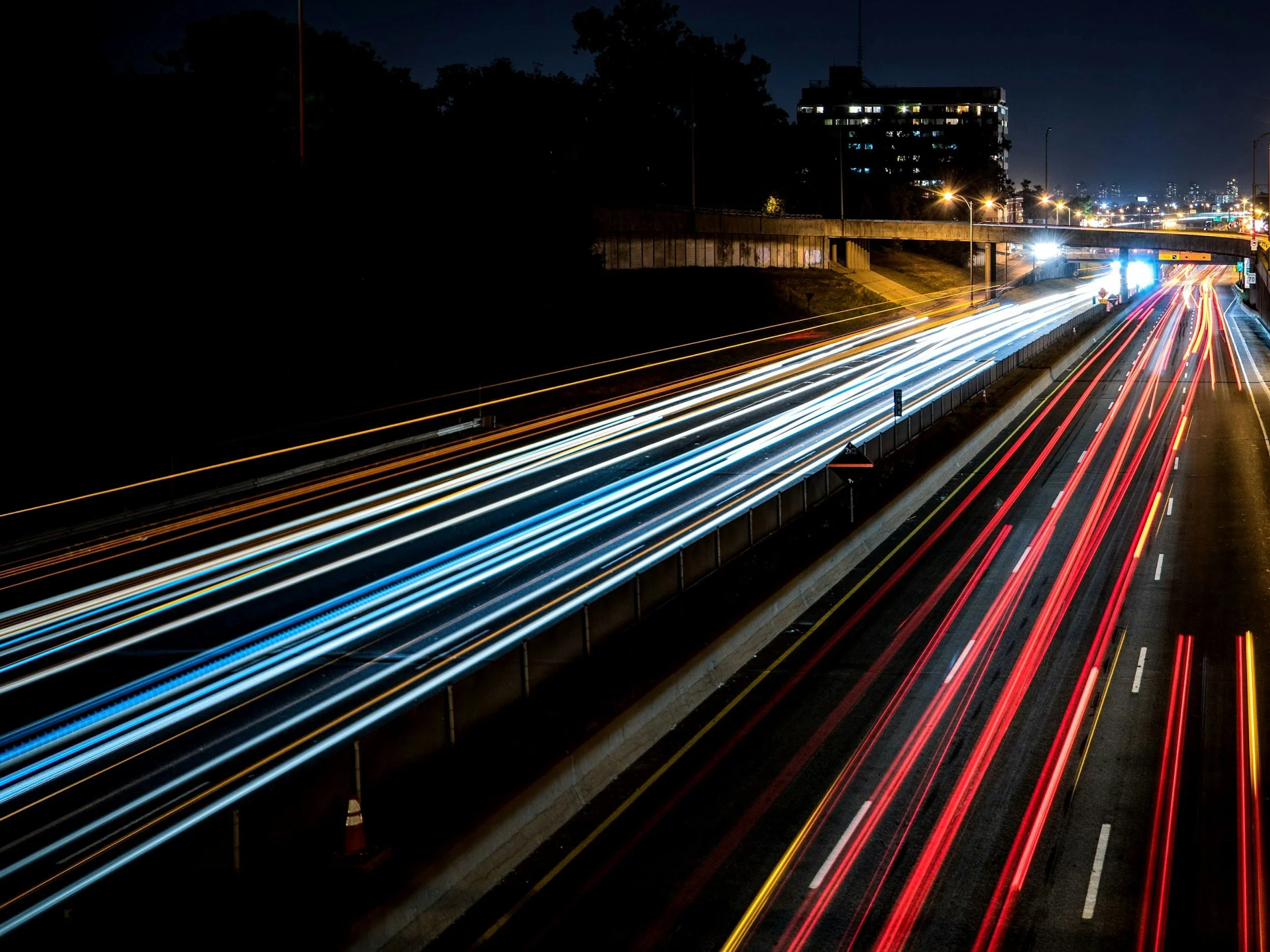 Nighttime highway with streaks of red and white light trails from moving vehicles, city lights and buildings in the background