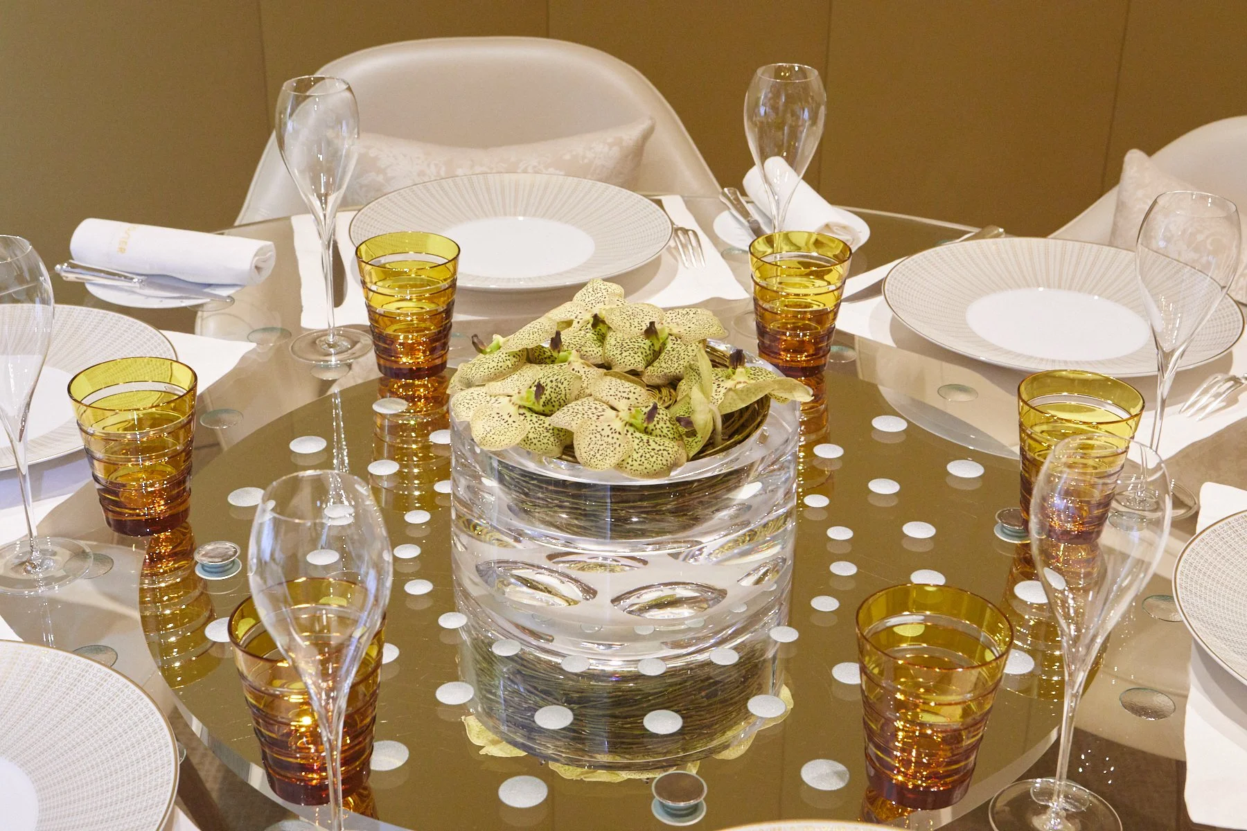 Restaurant table setting with minimalist floral centerpiece of orchids in a crystal vase surrounded by elegant dining ware.