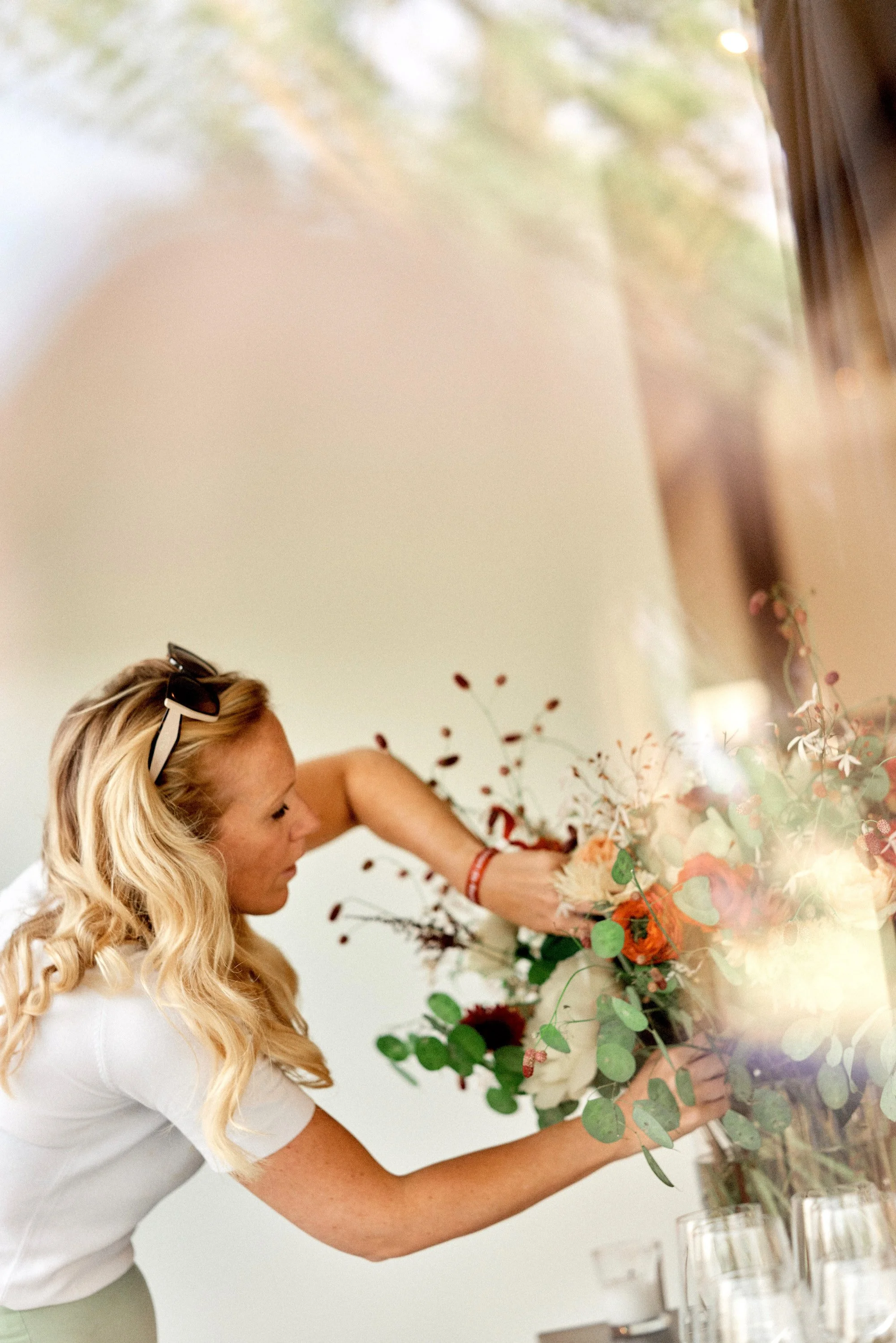 A woman with blonde hair placing a large bouquet of flowers on a table, seen through a mirror.
