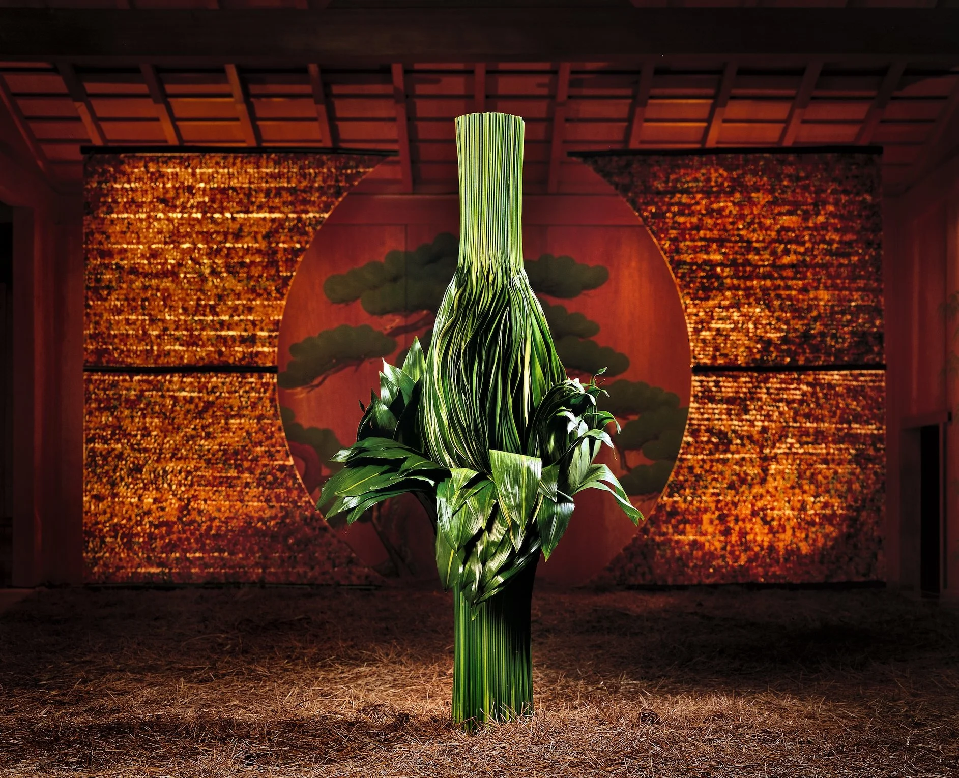Sculptural floral artwork made from layered green leaves, displayed against a golden Japanese theater backdrop.