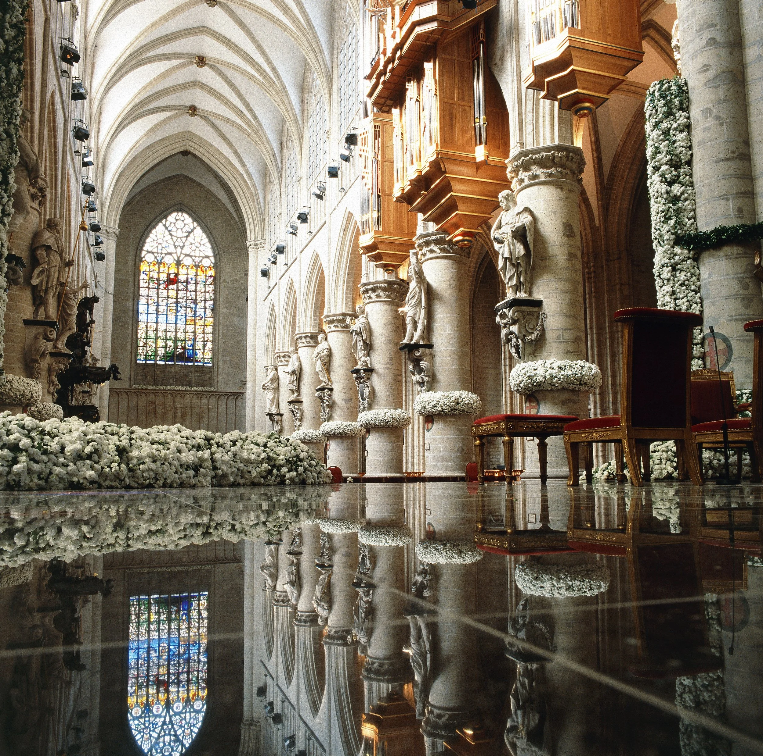 Cathedral wedding ceremony adorned with elegant white floral arrangements along columns, altar, and floor, blending heritage architecture with refined floral artistry by Daniel Ost.
