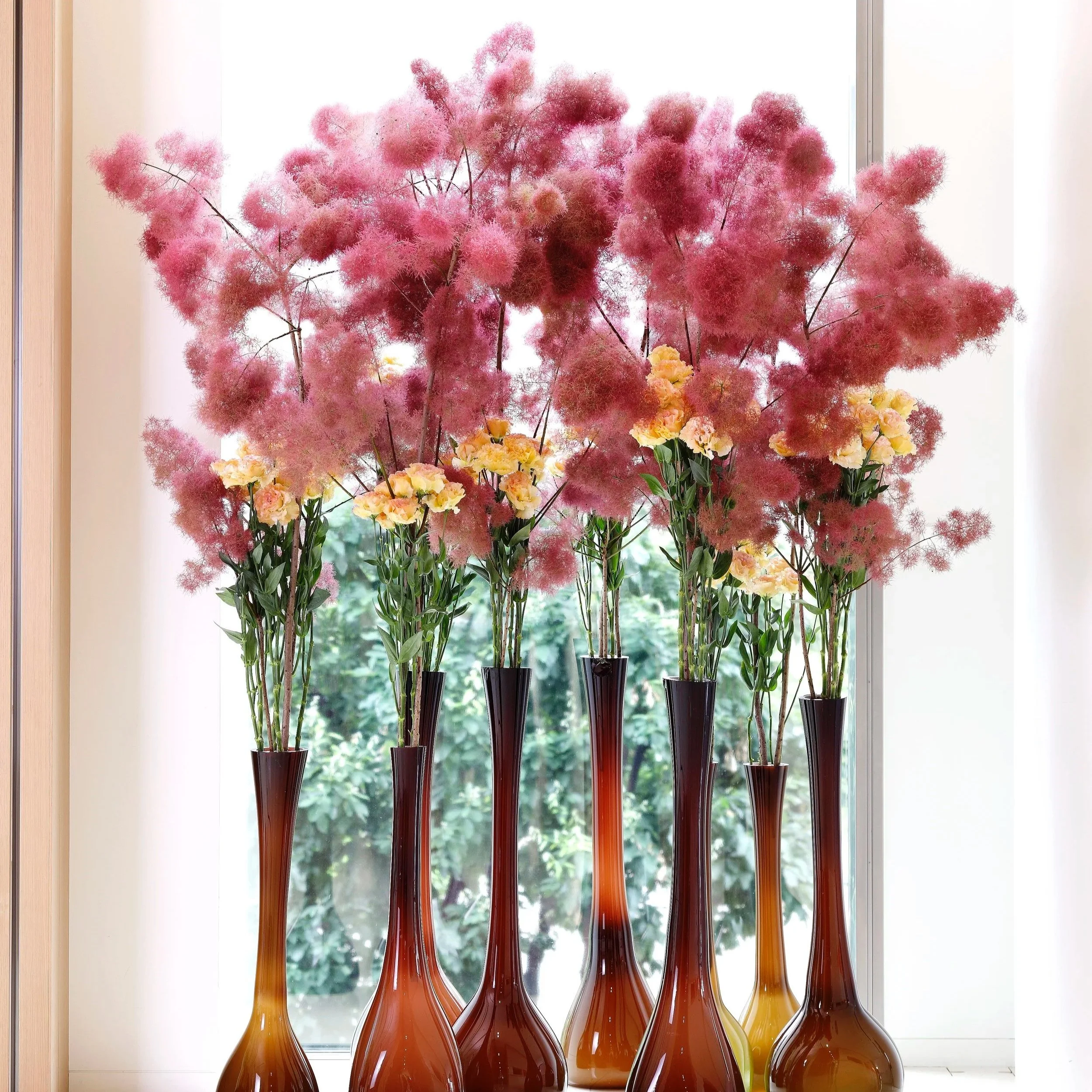 Daniel Ost floral display with pink smokebush and yellow flowers in tall glass vases.