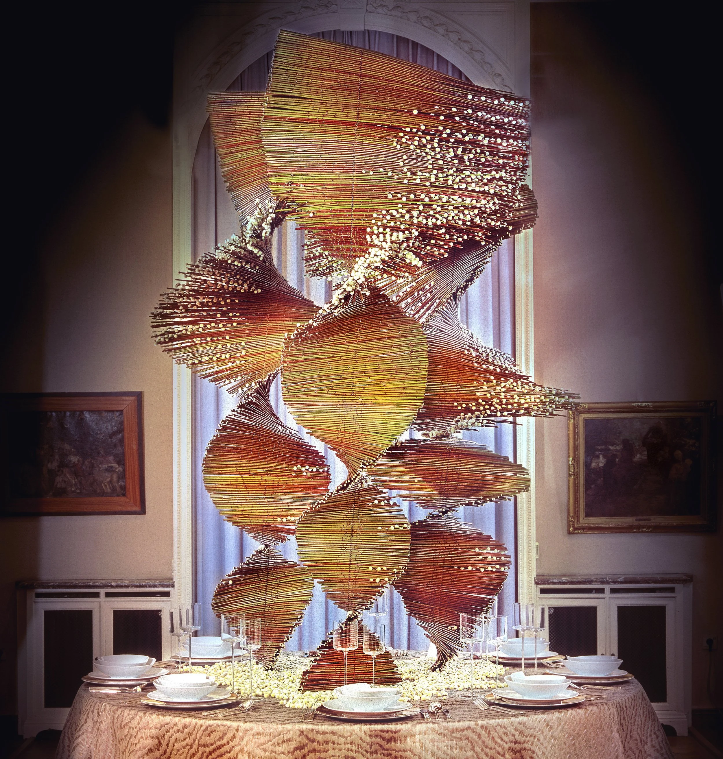 Architectural wedding table centerpiece featuring a dramatic spiral sculpture of golden twigs with delicate blossoms – modern sculptural floral design for luxury events.
