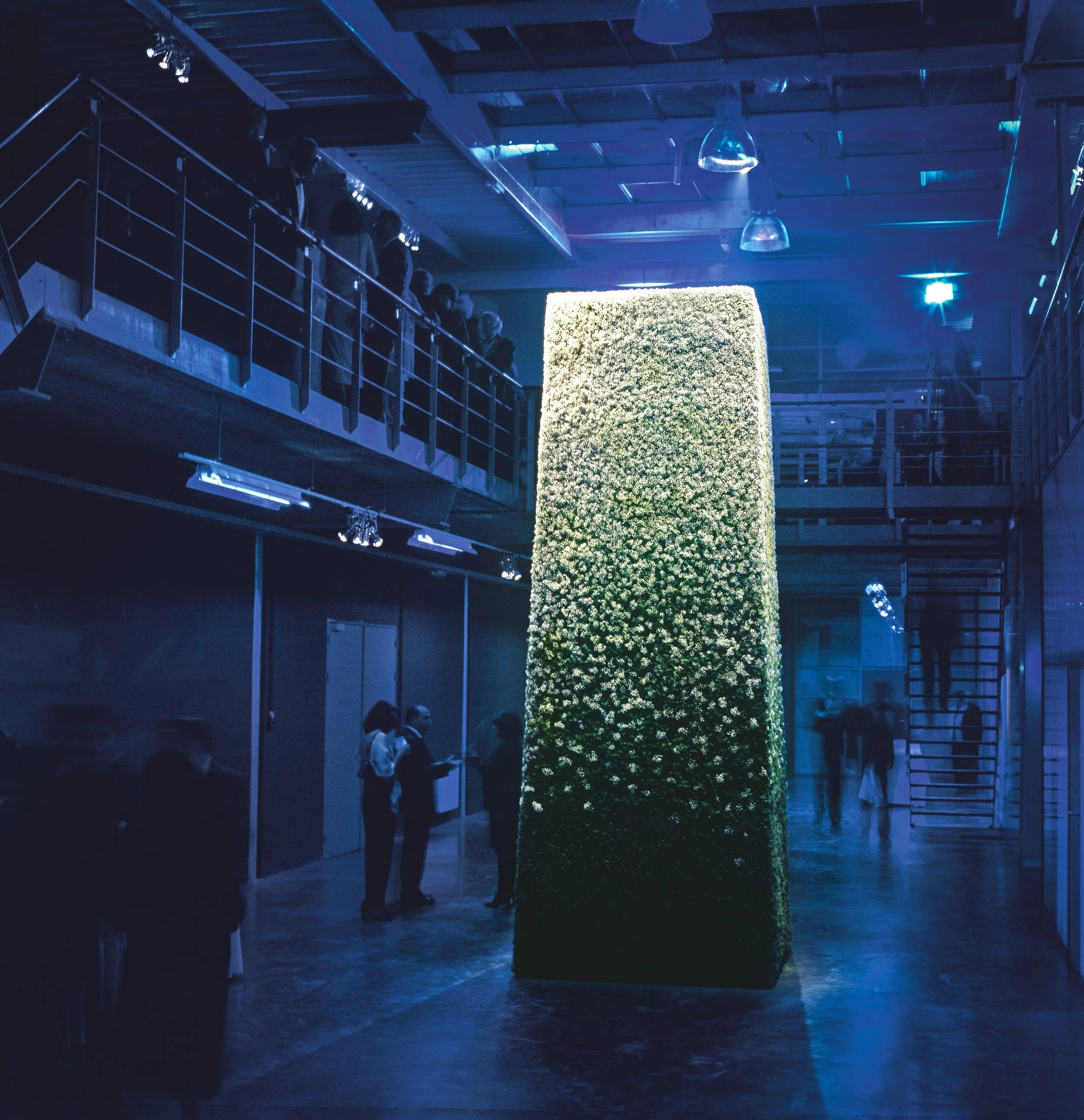 Contemporary corporate event featuring monumental green floral wall installation with ambient blue lighting.