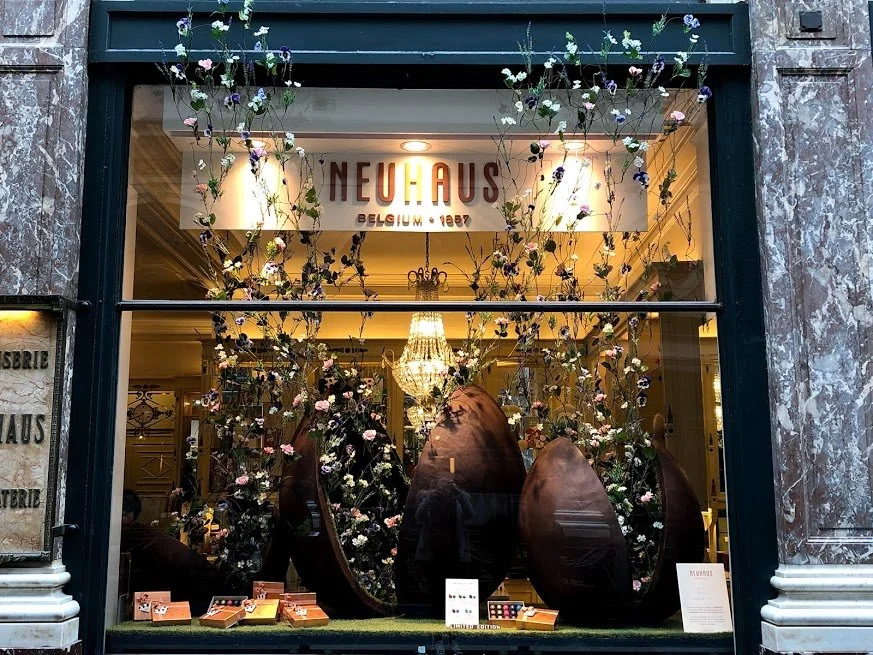 Window display for Neuhaus x Daniel Ost collaboration, featuring oversized chocolate eggs with cascading floral decorations in Galeries Royales Saint-Hubert.