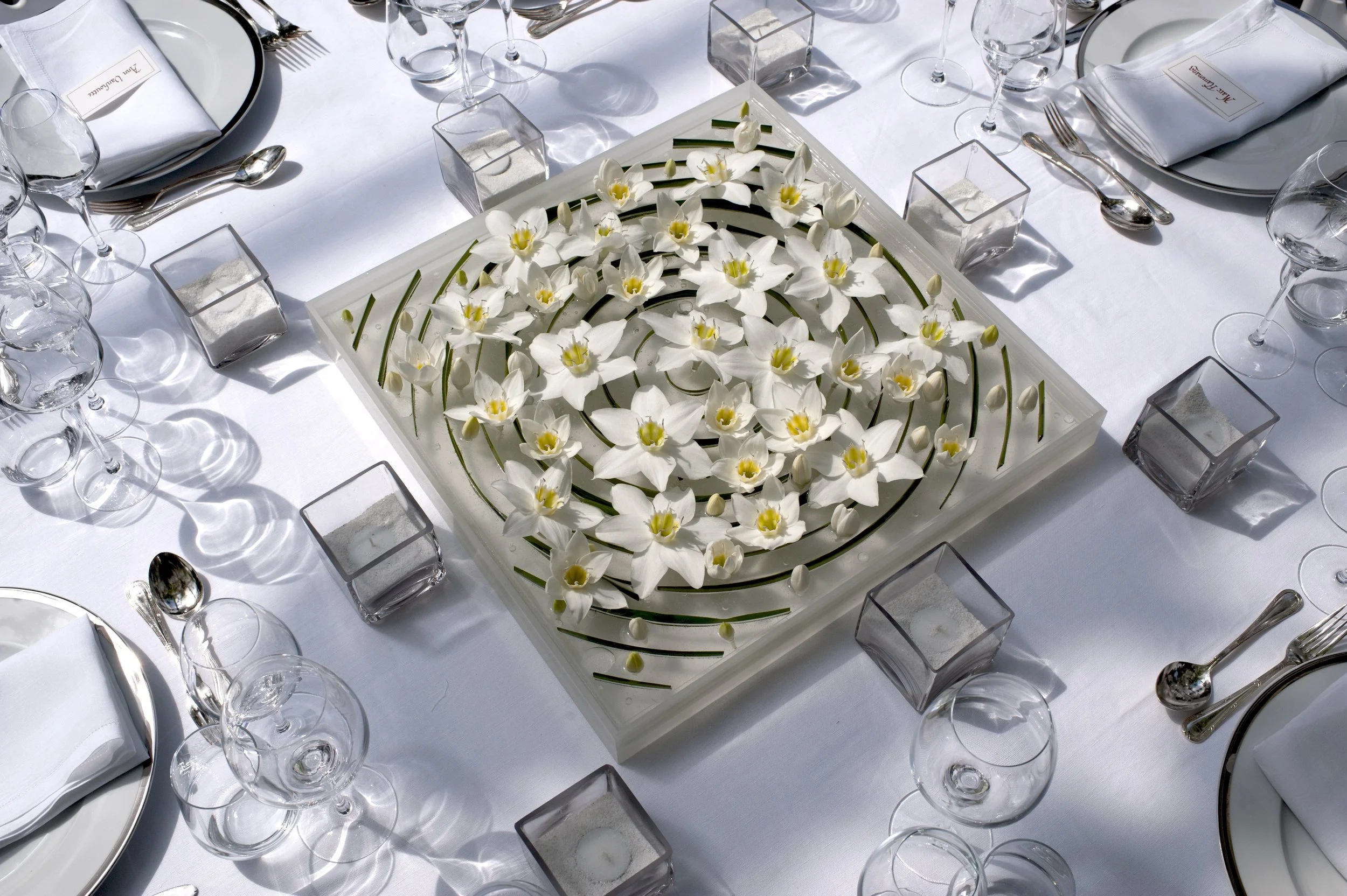 Elegant wedding table with a minimalist centerpiece of white flowers arranged in a spiral design, surrounded by crystal glassware and refined place settings.