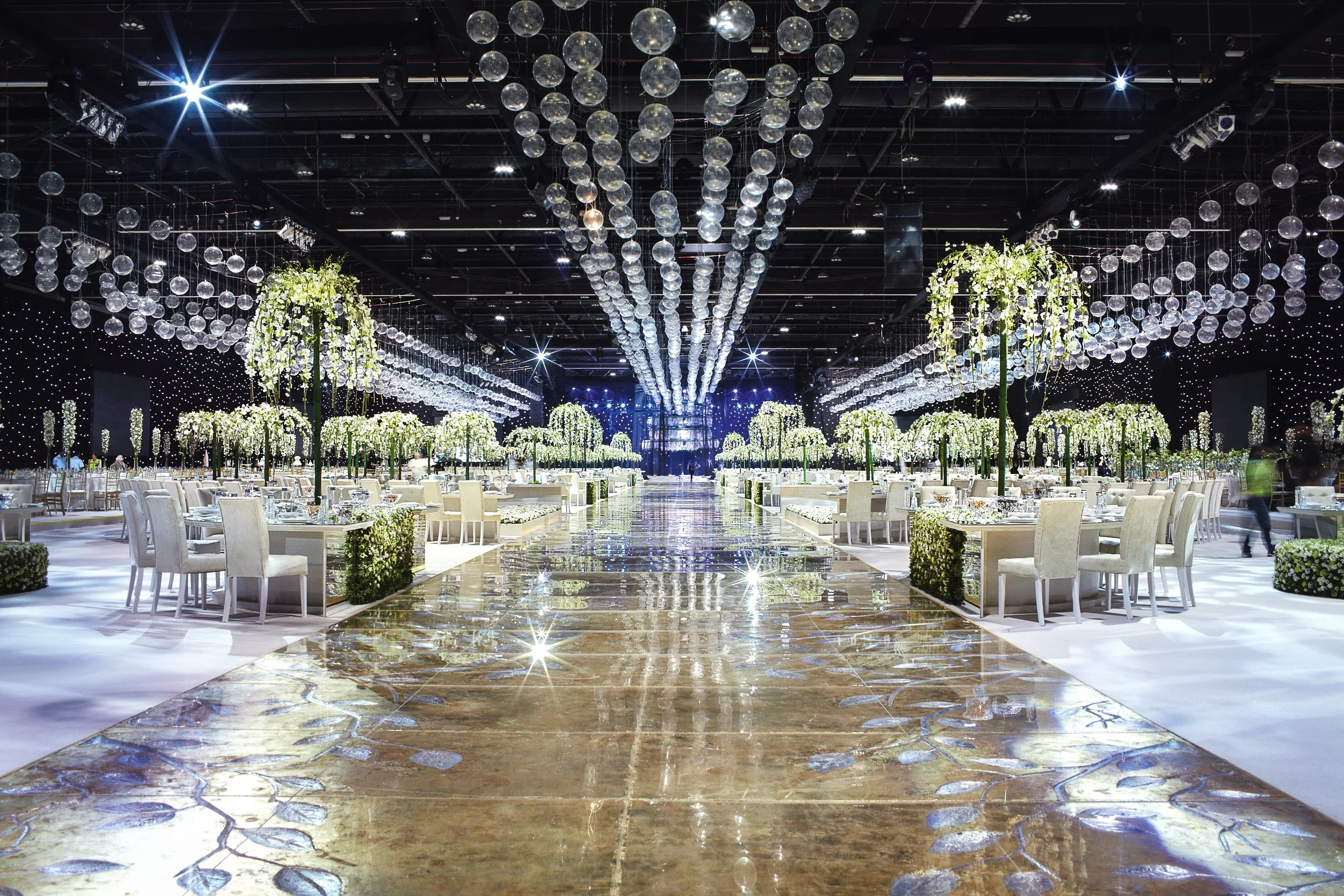 Elegant wedding reception with mirrored aisle, cascading floral chandeliers, and white floral tables by Daniel Ost.