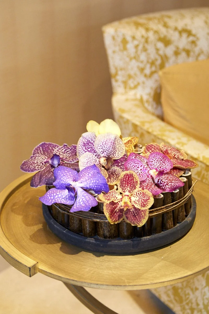Minimalist side table floral accent with vivid orchids in purple, yellow, and pink hues, styled for a luxury lounge setting.