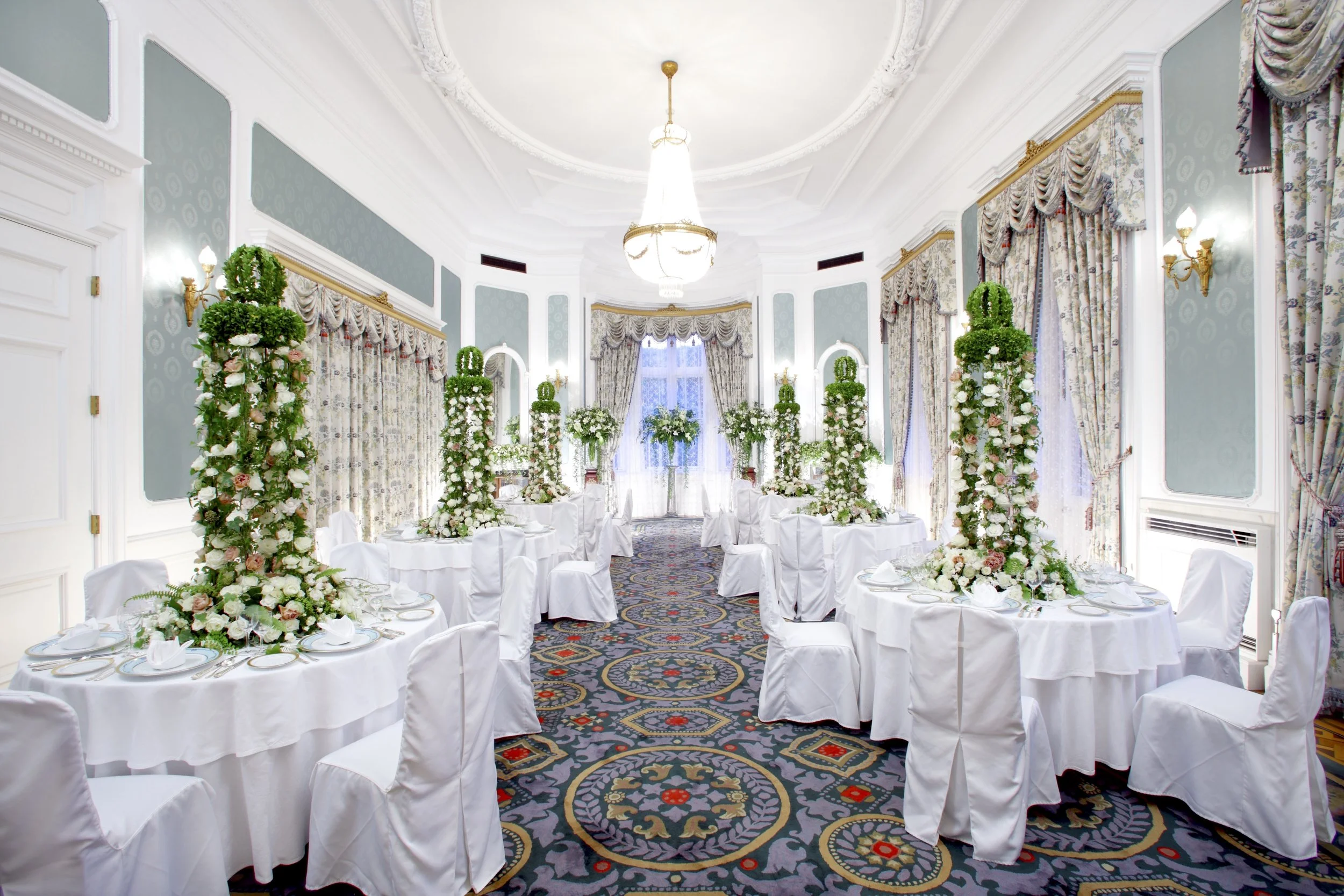 Regal wedding ballroom decorated with tall floral towers of roses and greenery, creating an intimate yet majestic dining experience.
