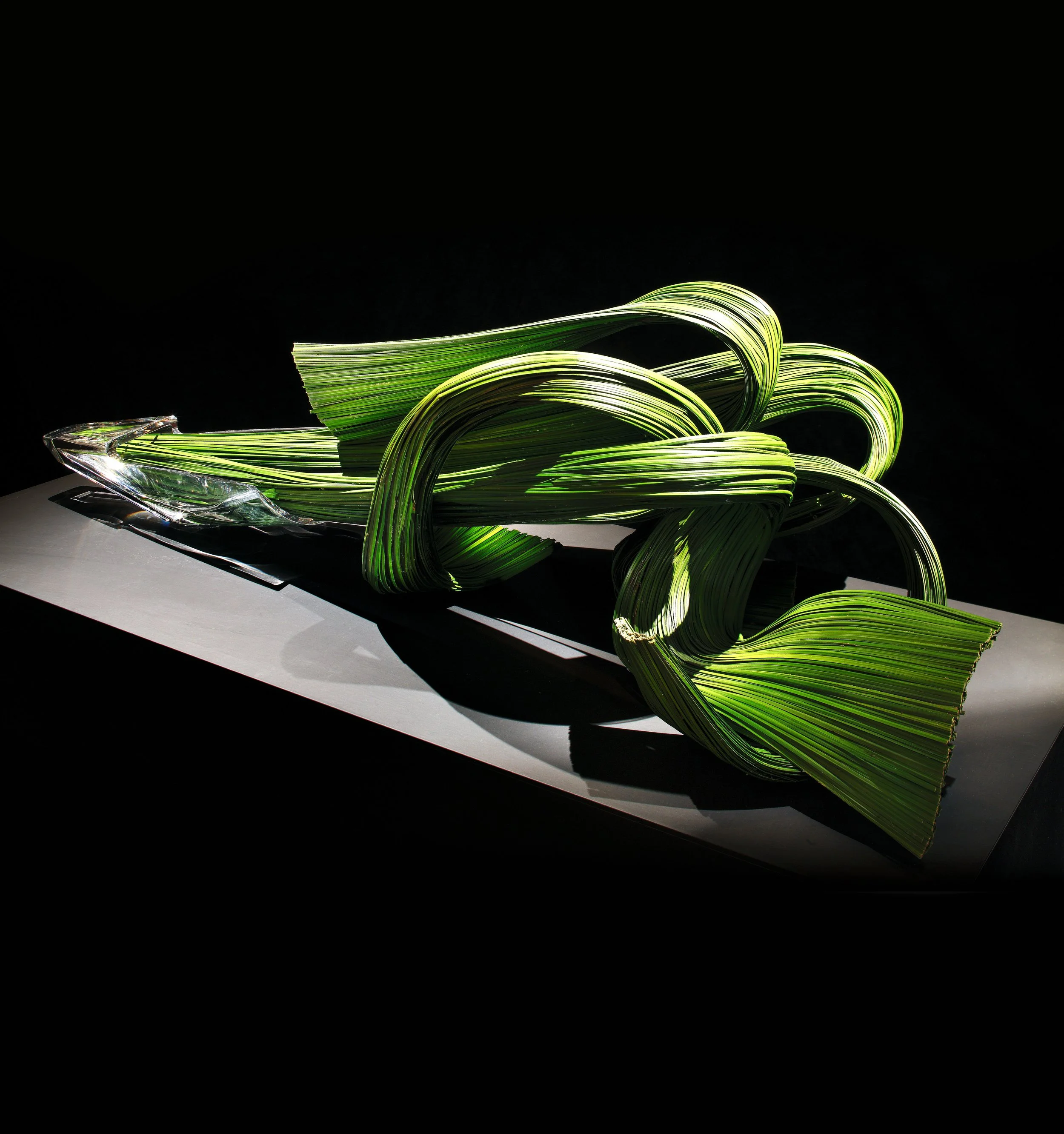 Avant-garde floral sculpture with woven green leaves in dynamic looping shapes displayed on a modern pedestal.