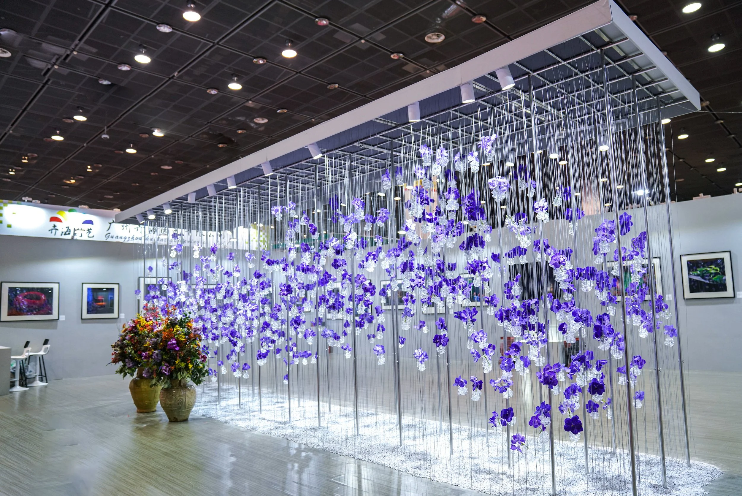 Suspended orchid flower installation with cascading purple blooms, creating an immersive floral art wall for an exhibition stand.