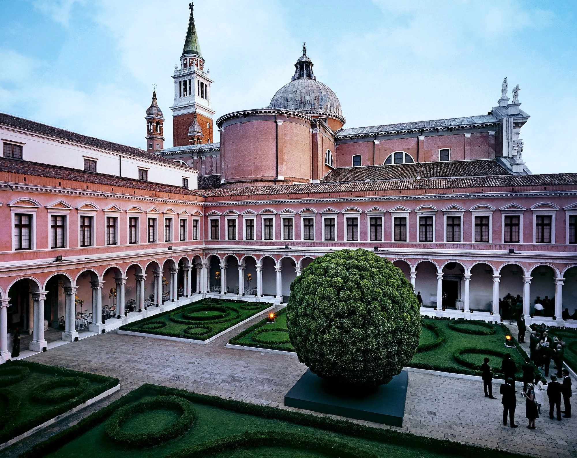 Historic cloister courtyard with geometric lawns, ornamental hedges, and a giant sculptural topiary sphere at the center.