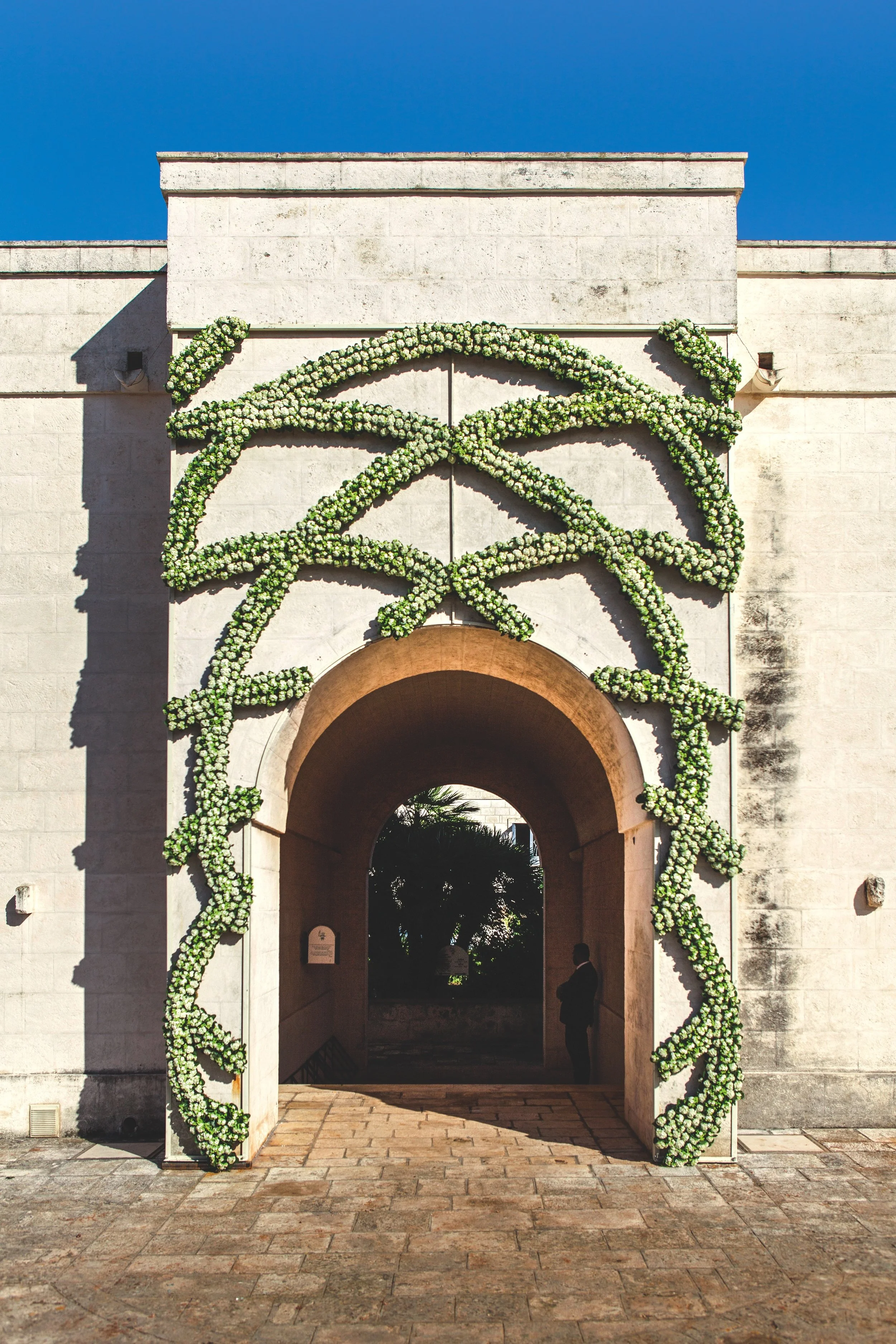 Luxury floral arch installation at a Mediterranean villa wedding, with sculptural white rose garlands adorning the stone entrance.