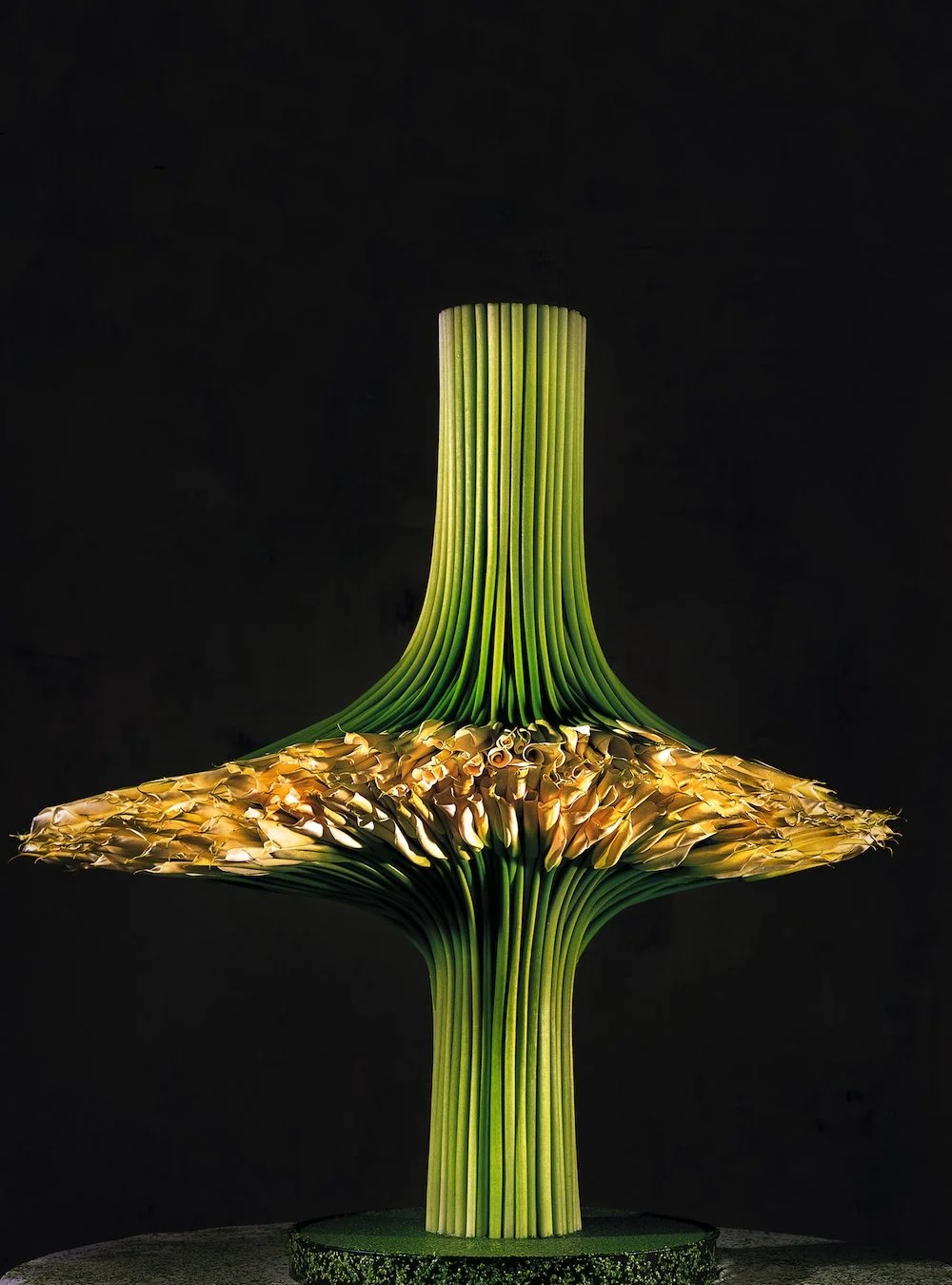 Architectural floral sculpture of structured green stems and curled yellow petals, resembling a modern organic totem.