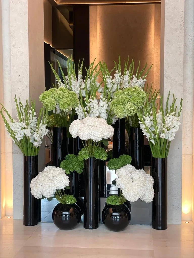 Hotel entrance floral installation with white hydrangeas, green hydrangeas, and gladiolus in black vases, styled for a modern luxury setting.as well