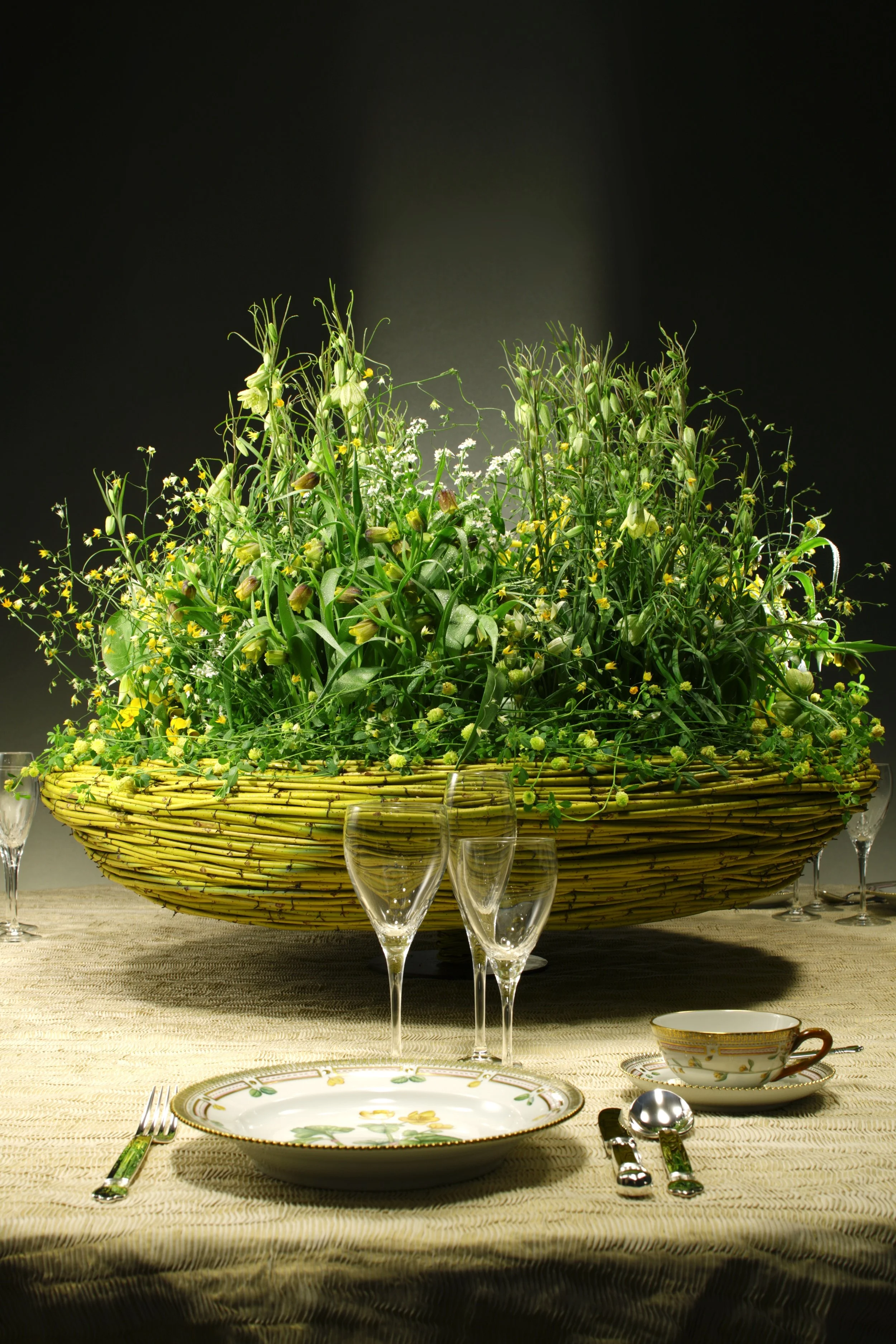 Creative wedding table decoration with a woven yellow basket overflowing with fresh greenery and delicate yellow flowers, evoking a natural garden setting indoors.