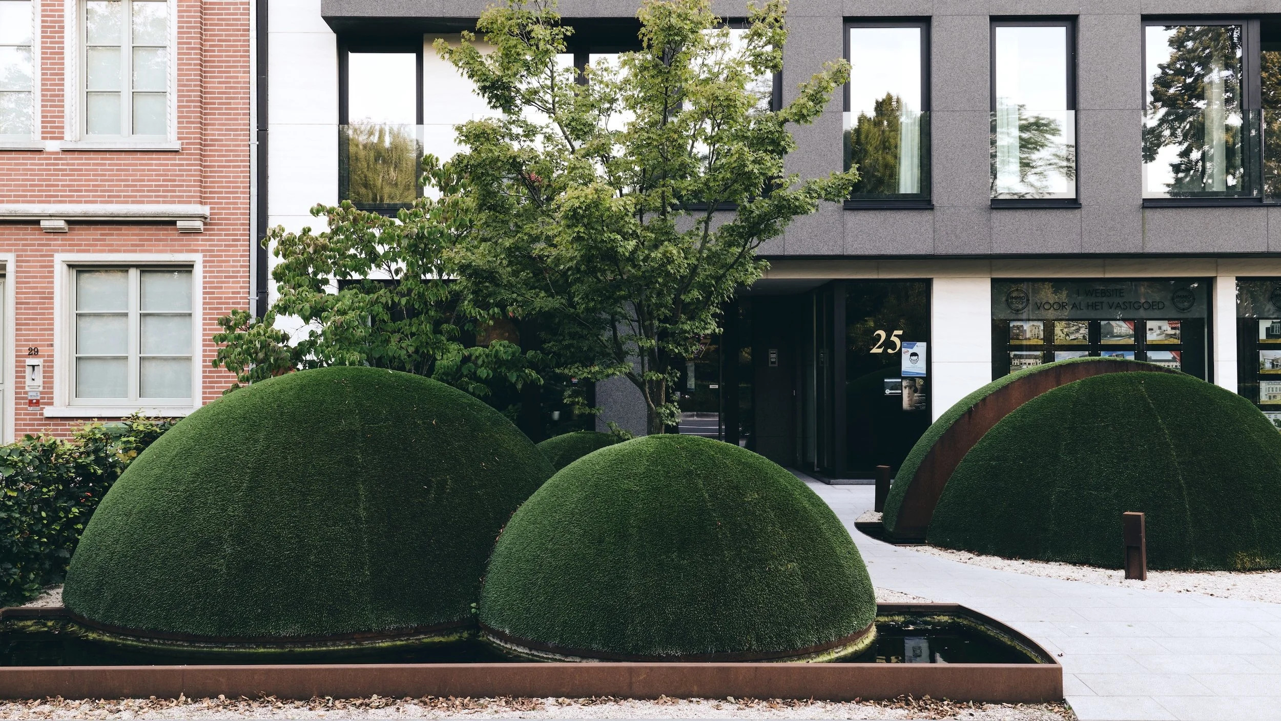 Contemporary townhouse with front garden featuring large dome-shaped topiary sculptures in a minimalist setting.