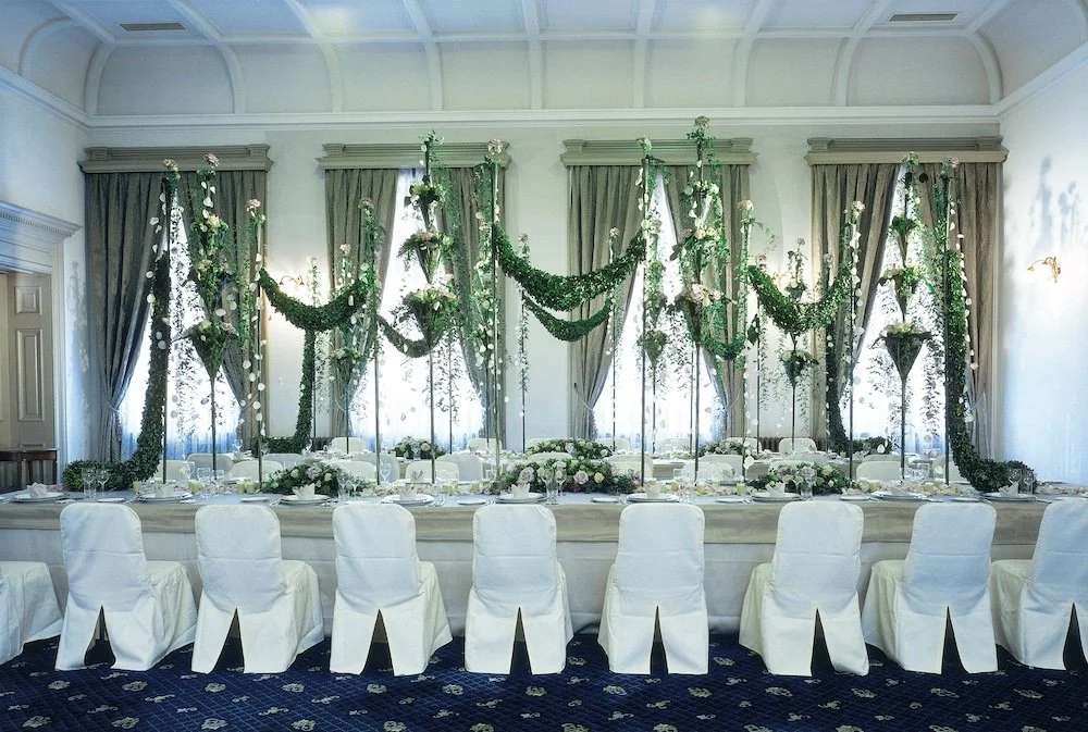 Romantic wedding long table decorated with tall floral columns, cascading greenery, and garlands, bringing elegance and intimacy to the reception hall.