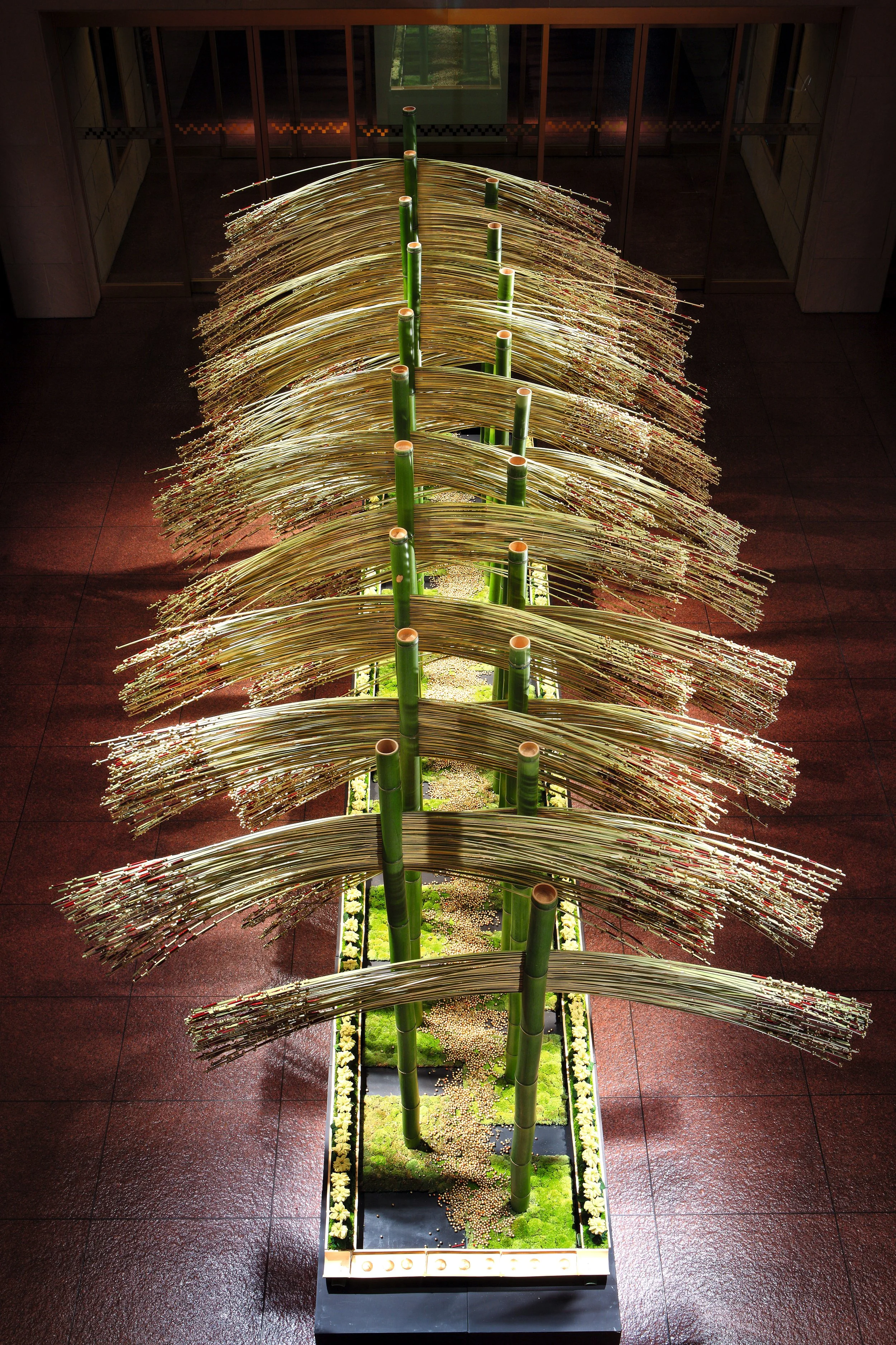 Indoor bamboo sculpture installation with bamboo stalks and curved metallic elements, mounted in a long planter with moss and small plants, in a modern building lobby.