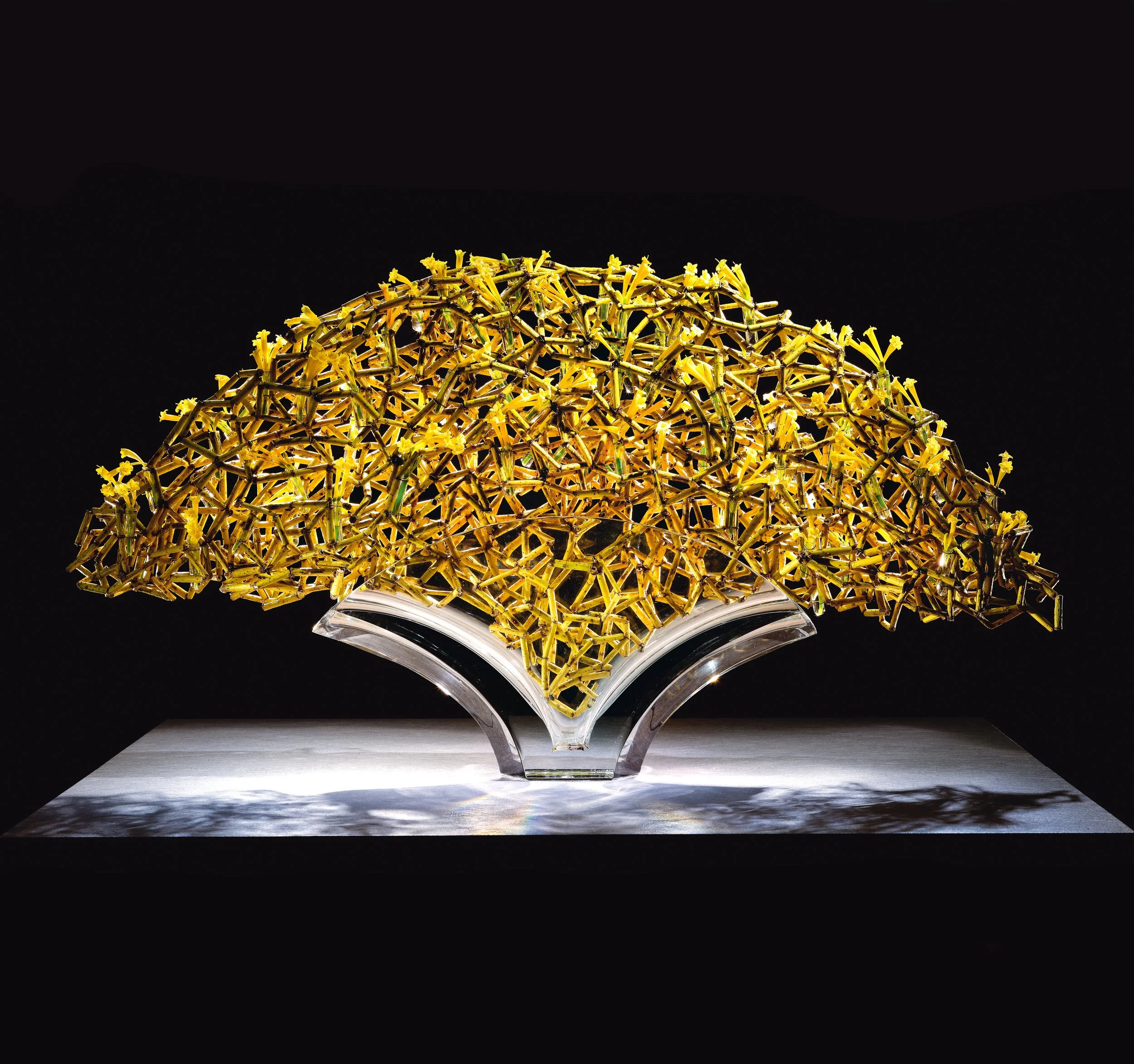 Sculptural yellow floral artwork with hundreds of blossoms interwoven into a geometric arch form on a glass structure.