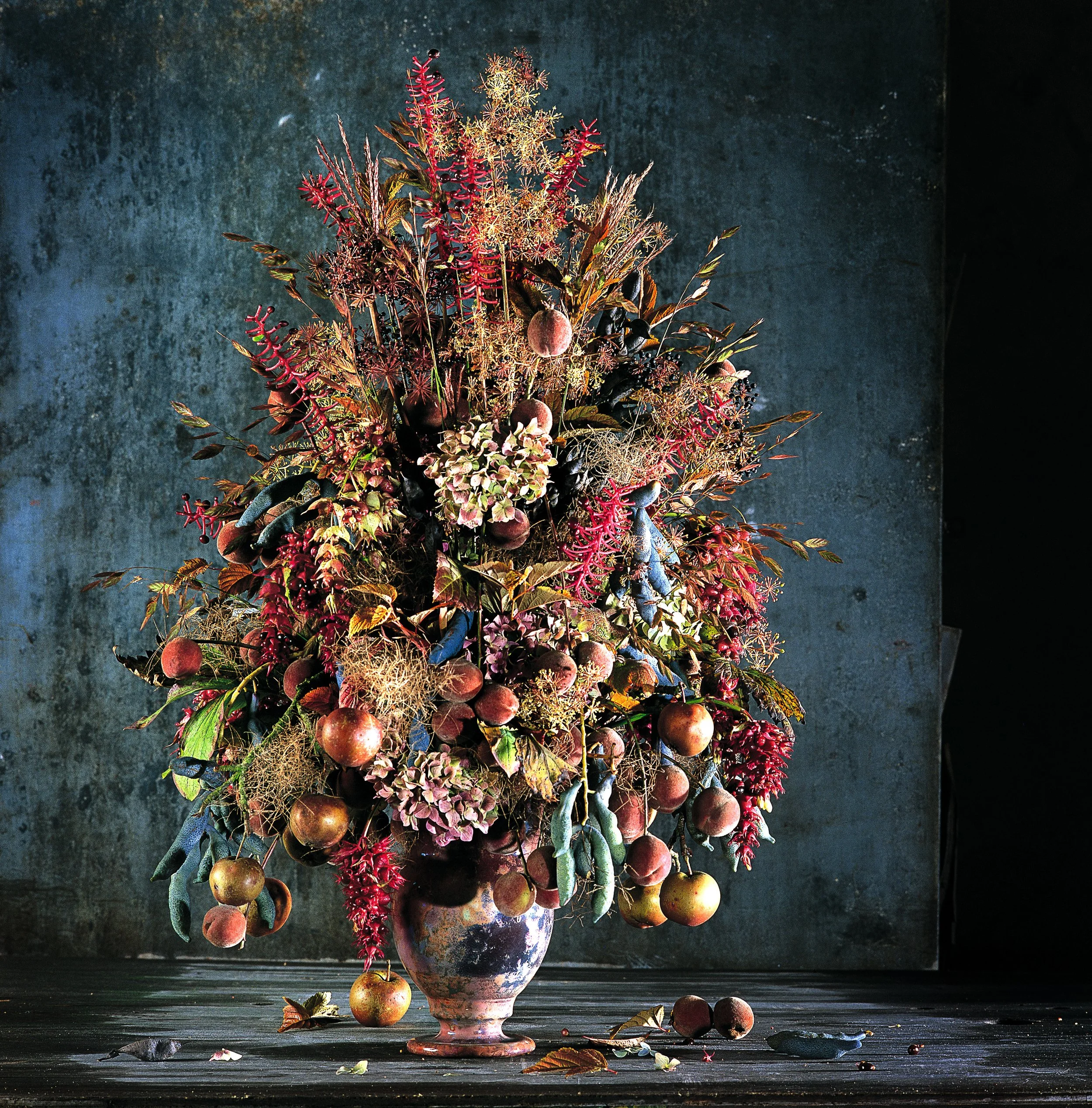 Opulent floral arrangement with peaches, hydrangeas, and autumn branches in a rustic urn, styled in a painterly still-life manner.
