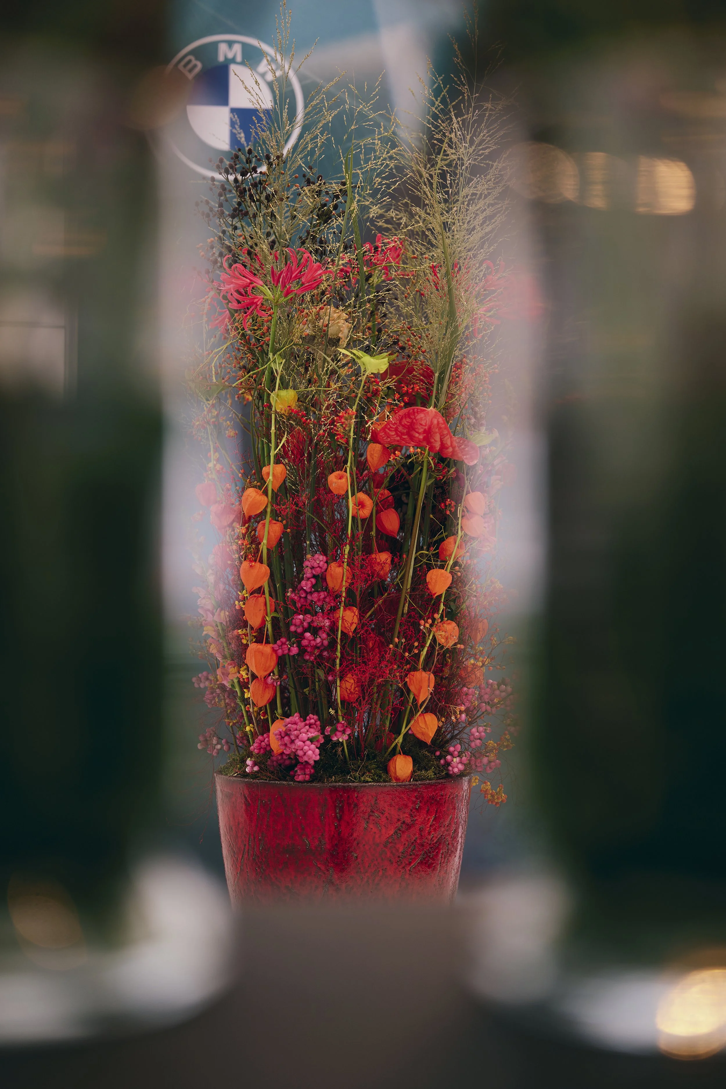 Vibrant corporate floral arrangement with red, orange, and pink blooms in a tall vase, styled for a BMW brand event.