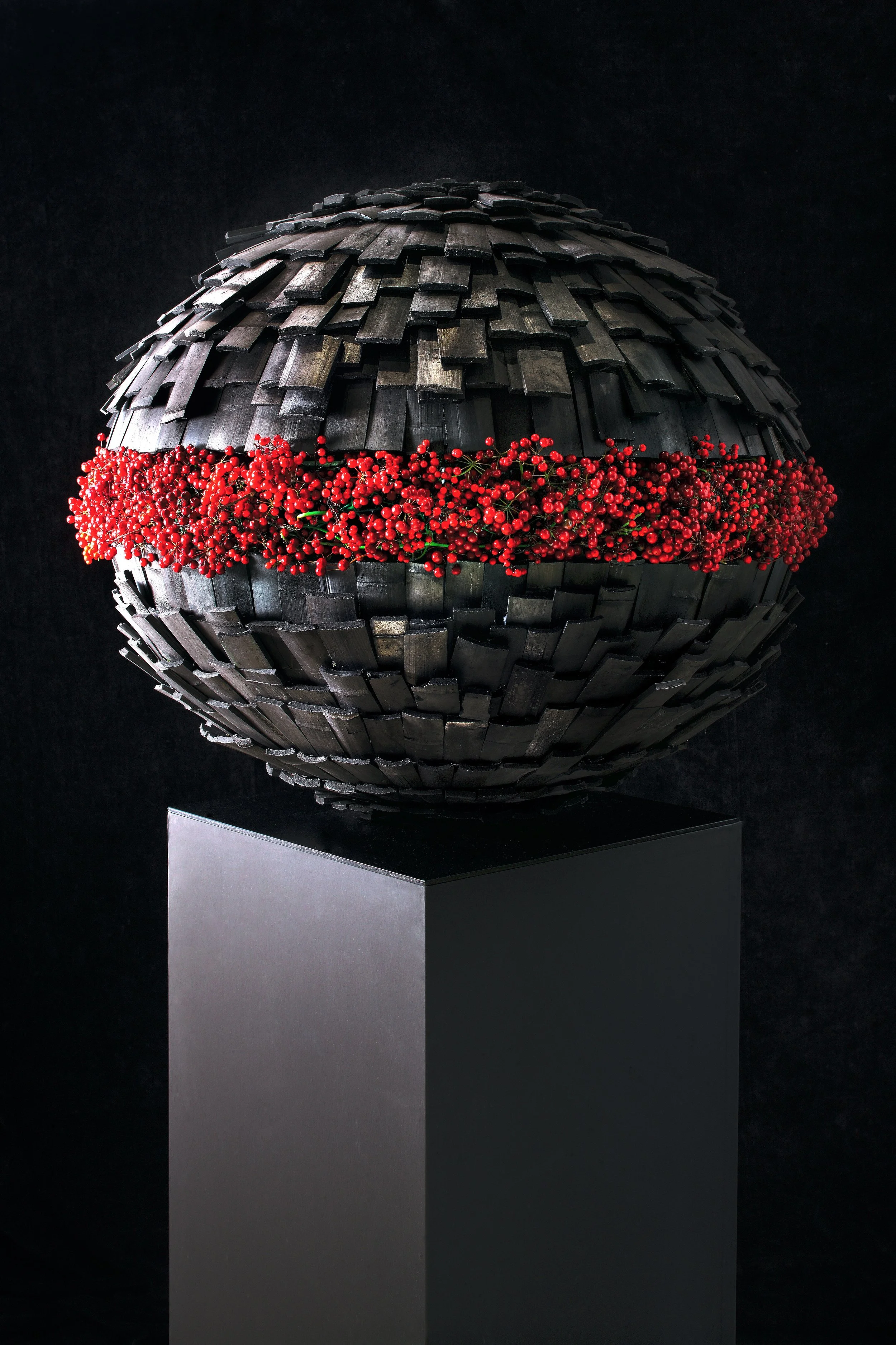 Spherical floral art installation with a black wooden shingle structure encircling a vivid red floral band.