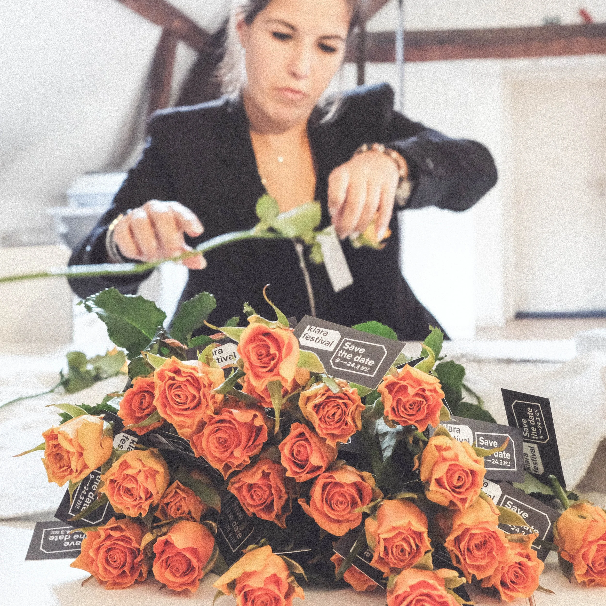 Florist preparing orange rose bouquets with “Klara Festival” save-the-date cards for an artistic promotional campaign.