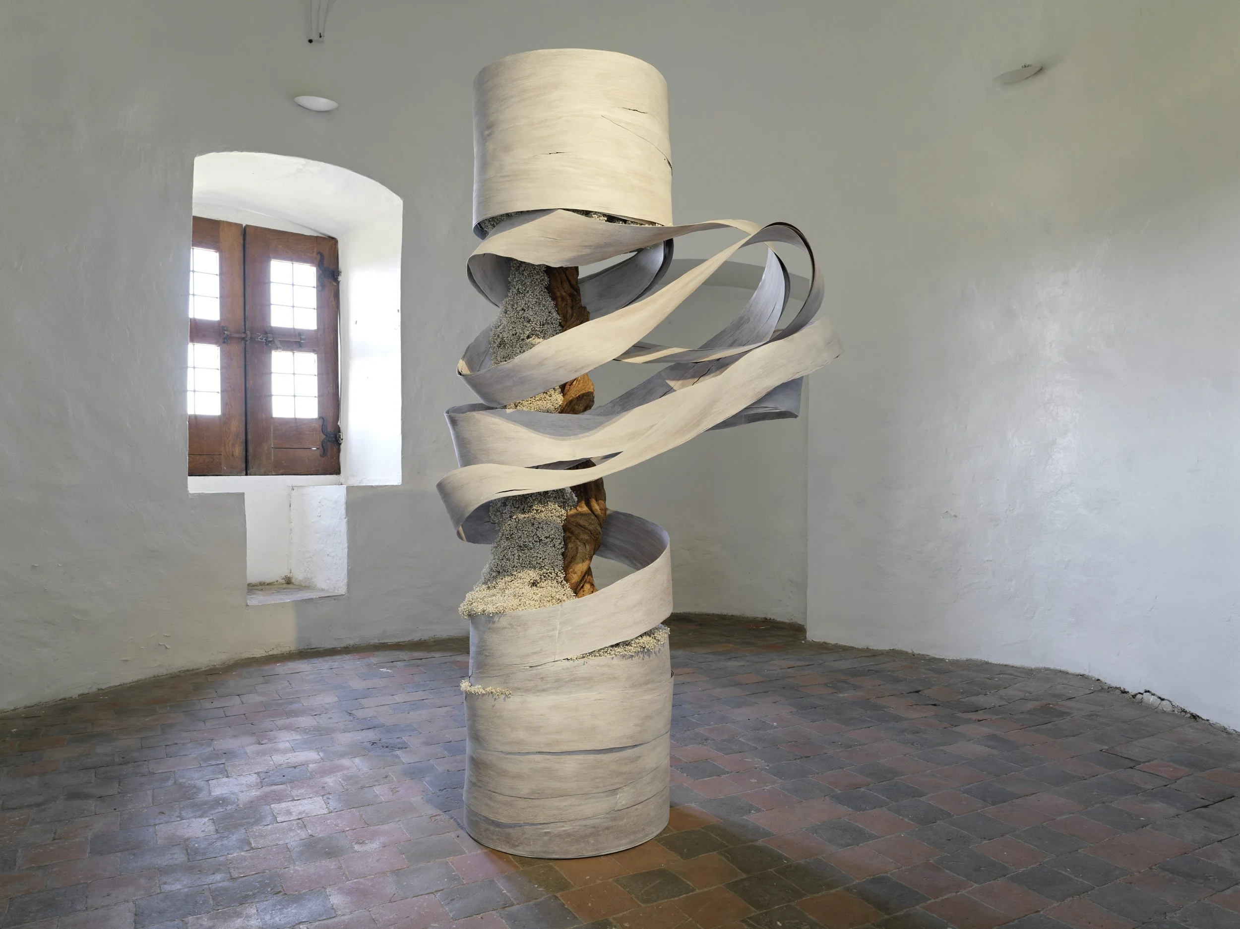 Architectural floral sculpture made of natural materials and wood spirals, displayed in a historic whitewashed interior with stone flooring.