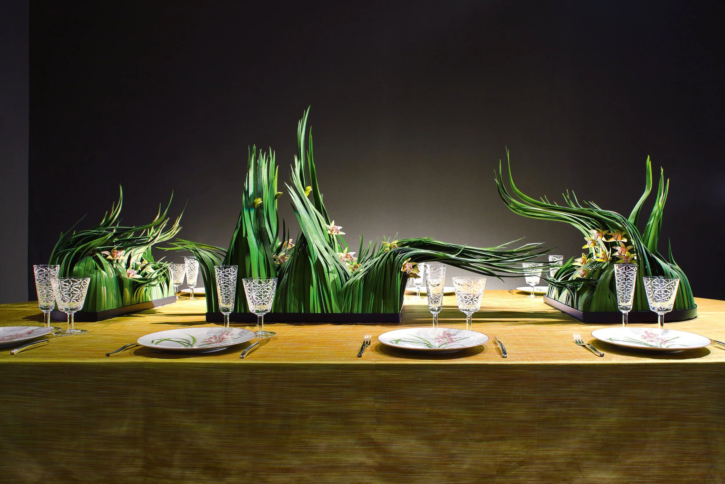 Contemporary wedding table decoration with sculptural green leaves and delicate orchids sweeping across a long dining table – artistic floral design by Daniel Ost.