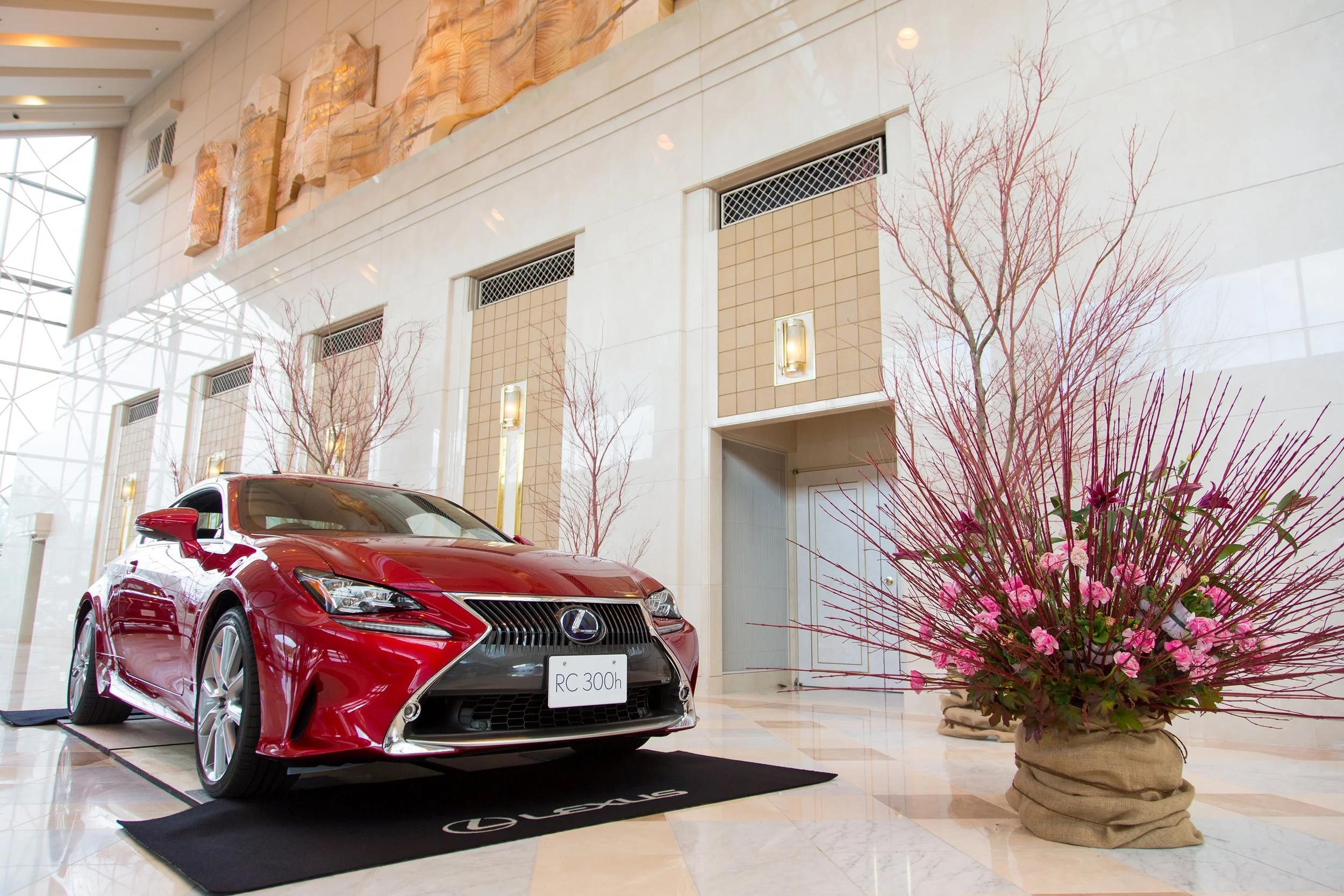 Floral styling for Lexus car launch, featuring a red Lexus RC 300h with bold pink floral arrangements in a luxury showroom.