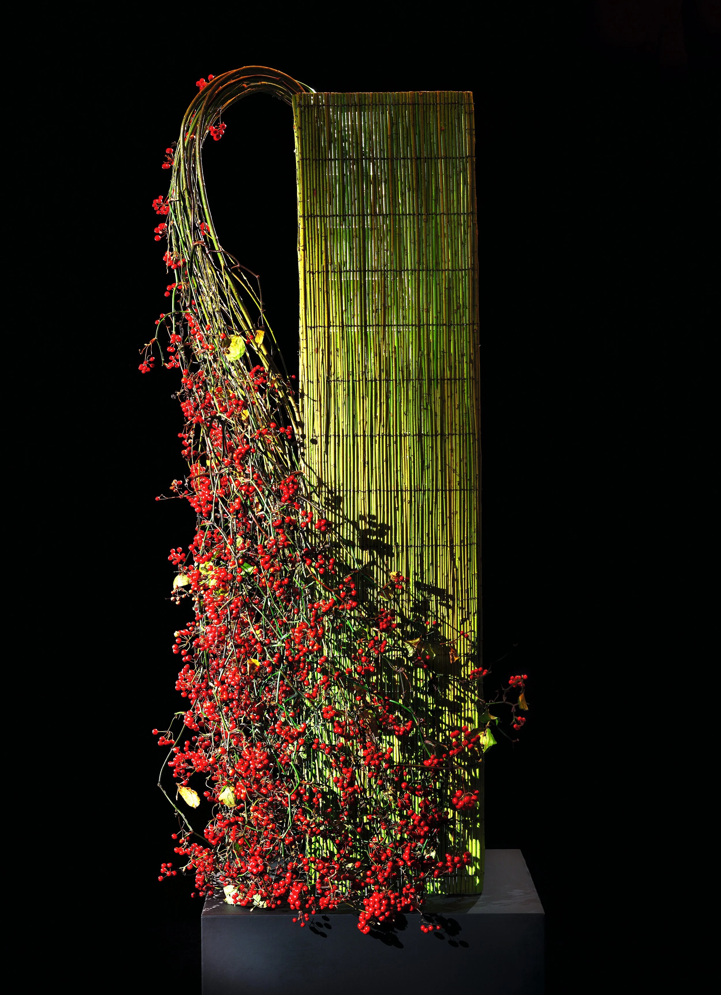 Architectural green bamboo panel installation with cascading red berries spilling gracefully to one side.