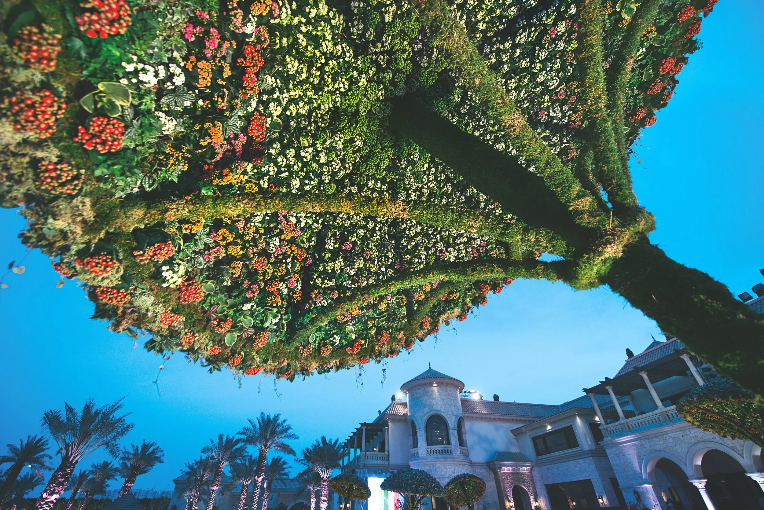 Outdoor wedding celebration under sculptural floral tree canopies, covered with colorful blossoms and greenery, blending nature and architecture in a luxury villa setting.