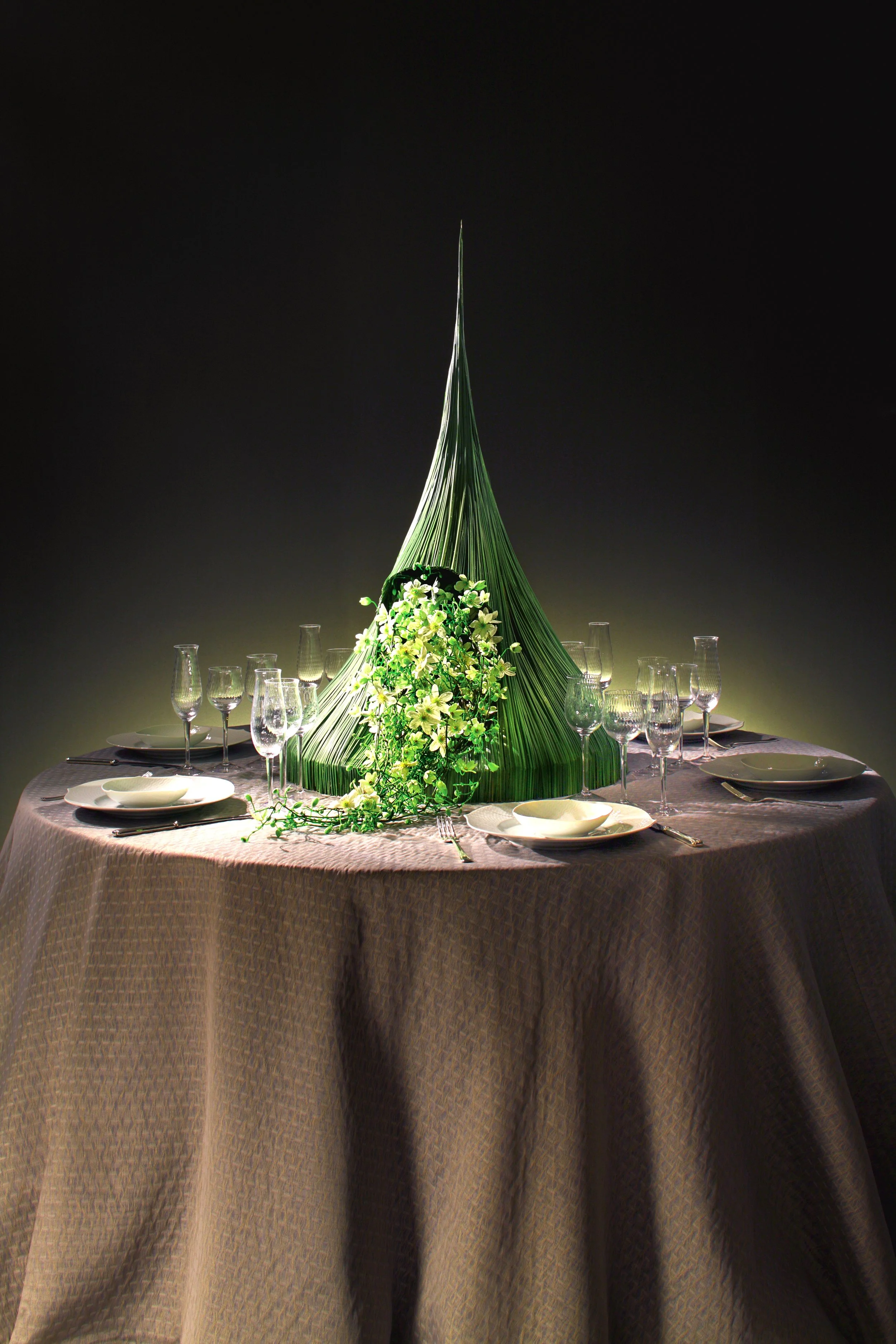 Artistic wedding table centerpiece with a tall green sculptural cone and cascading white flowers, creating a modern and elegant floral installation.