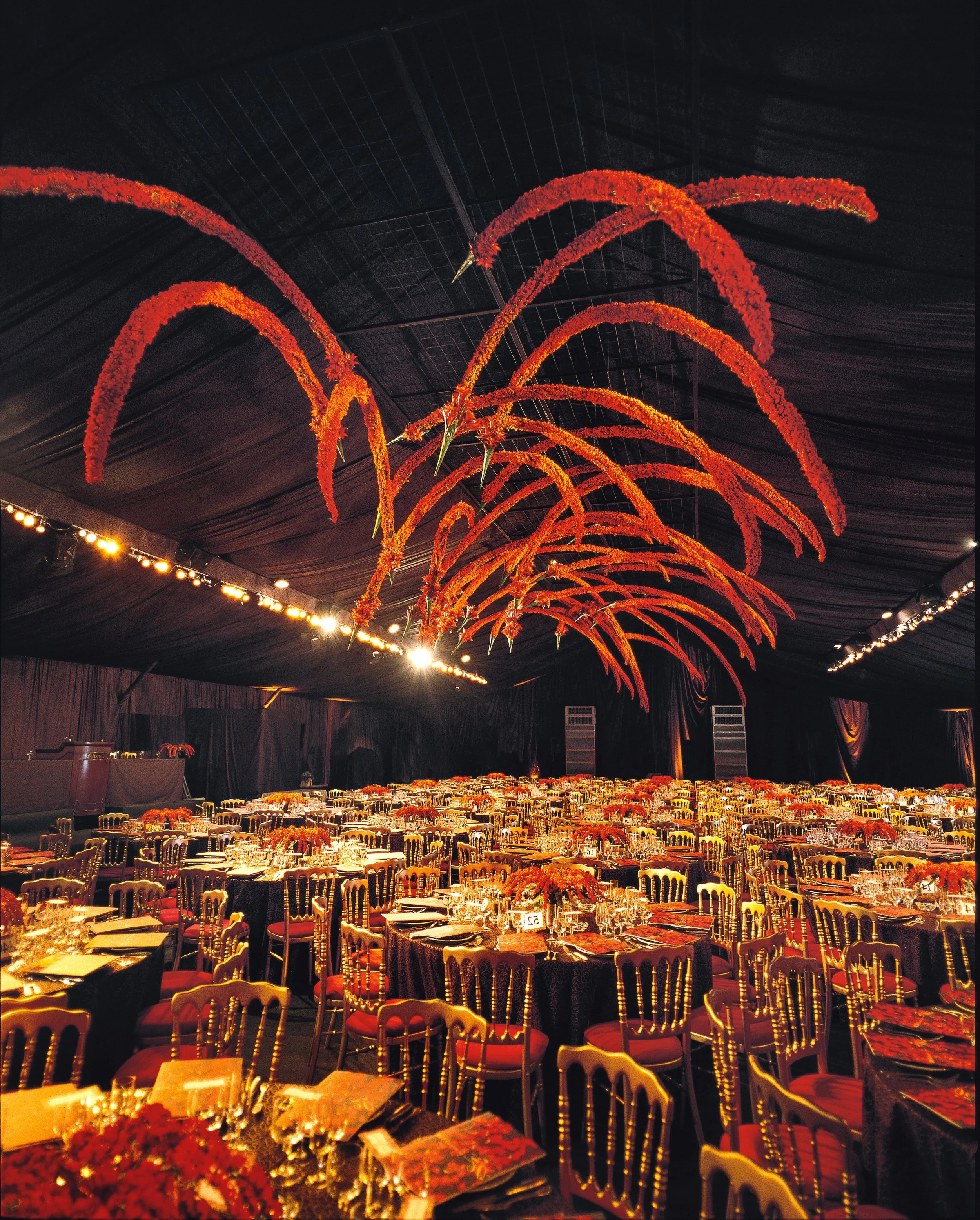 Luxury corporate gala with bold red floral ceiling installation and gold dining setup by Daniel Ost.