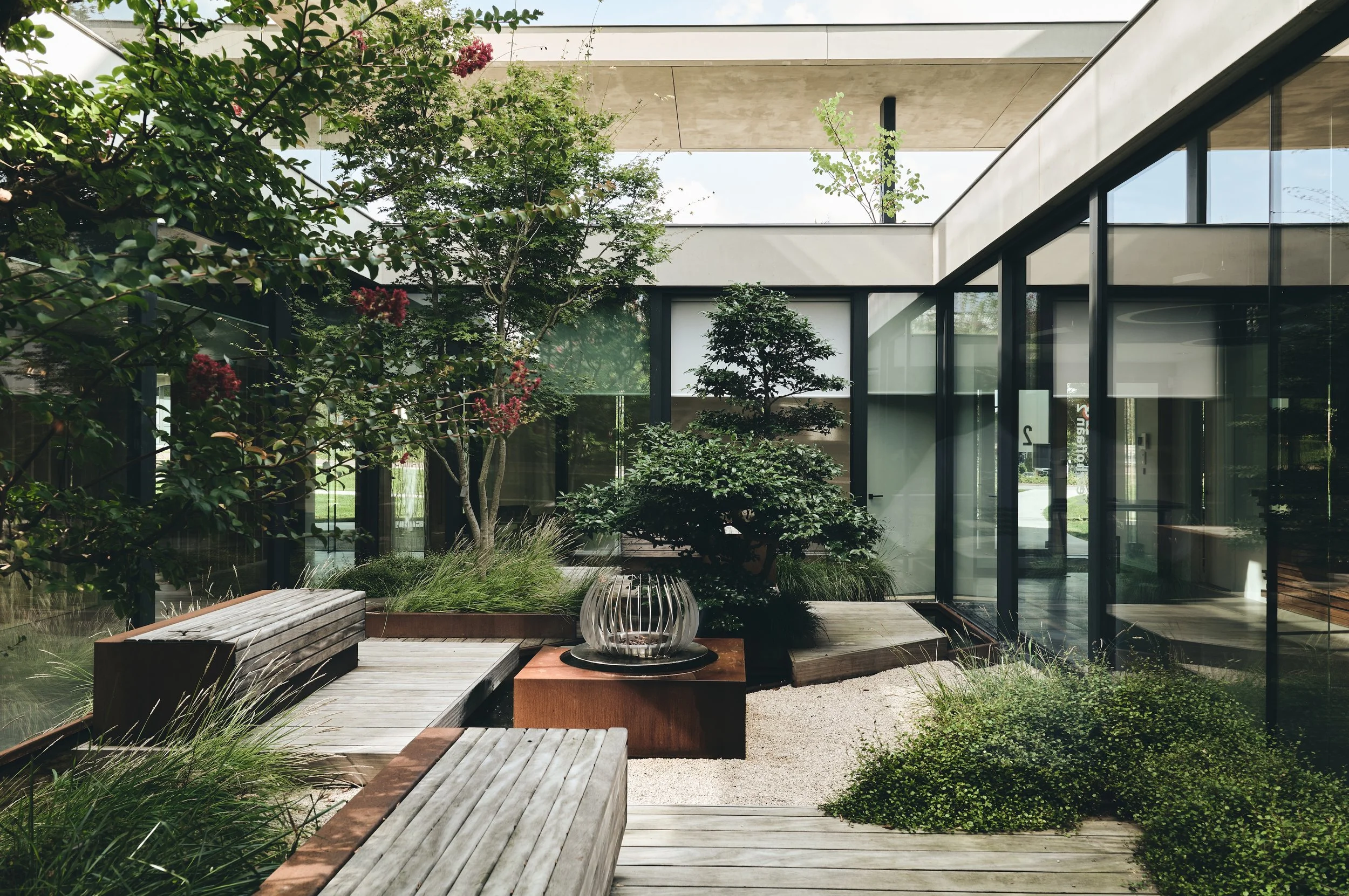Minimalist courtyard garden in a contemporary office building with bonsai, ornamental grasses, and integrated wooden seating.
