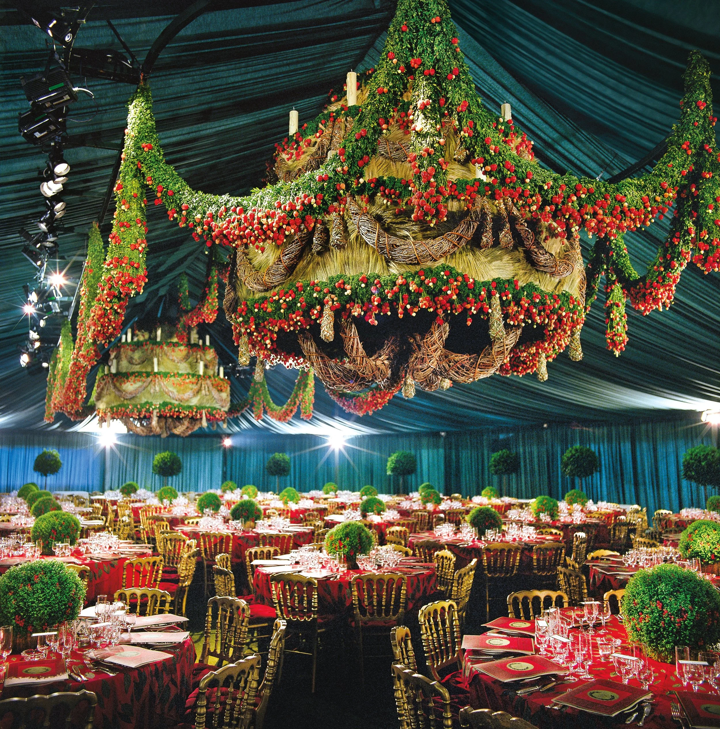 Festive corporate event with opulent chandeliers draped in red berries and greenery above banquet tables, Daniel Ost grand floral creation.