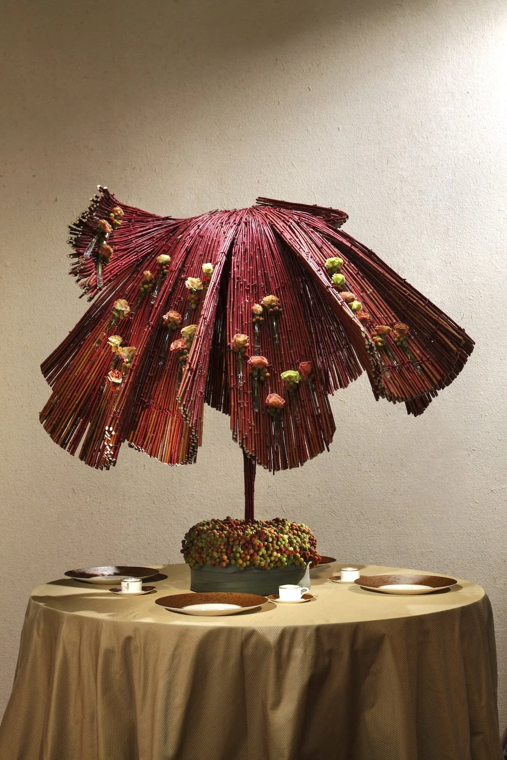 Luxury wedding table arrangement featuring a dramatic sculptural red willow umbrella centerpiece with fresh flowers, designed to create an intimate and artistic dining atmosphere.