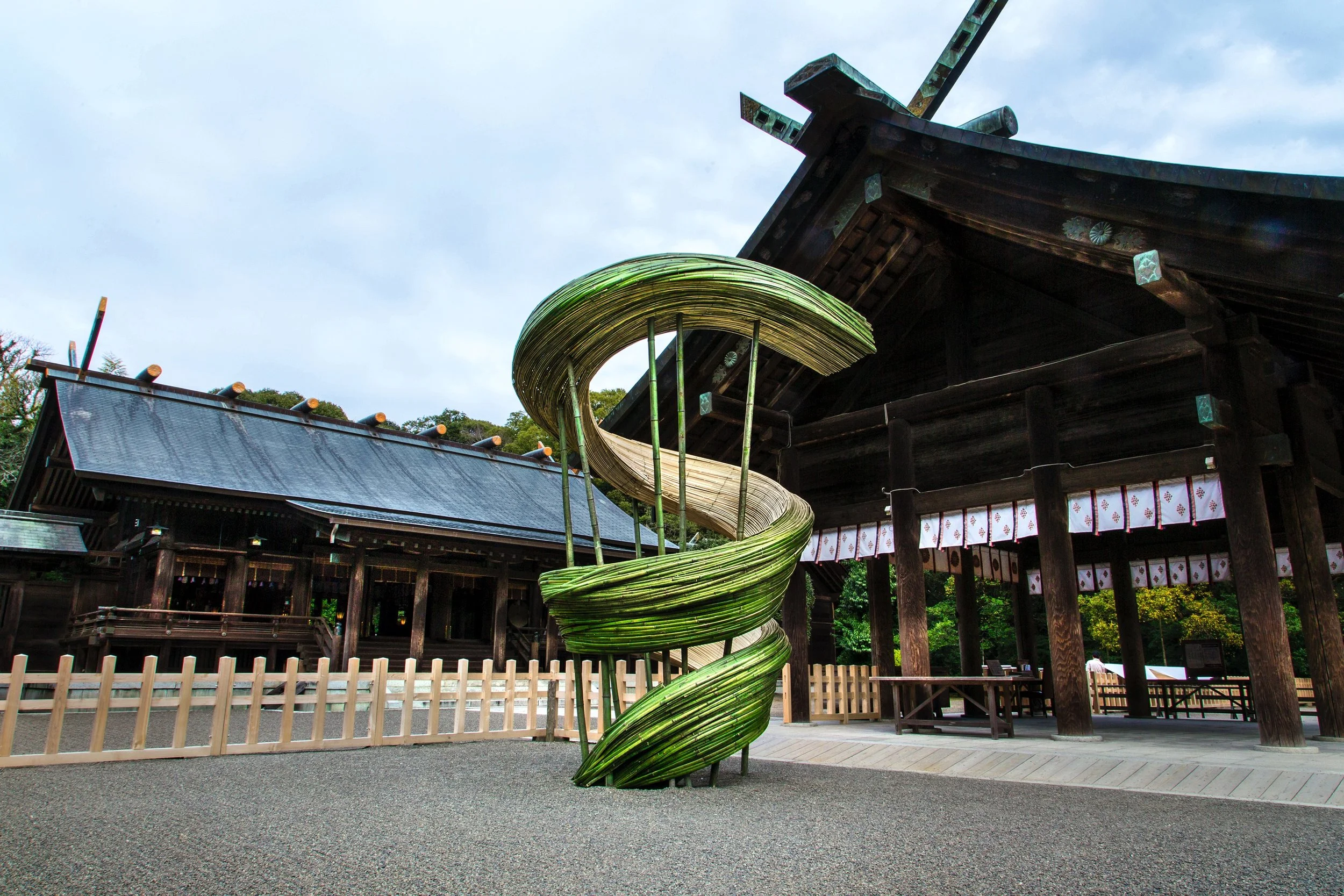 Architectural floral sculpture in spiral form made of green natural materials, displayed at a Japanese temple courtyard.