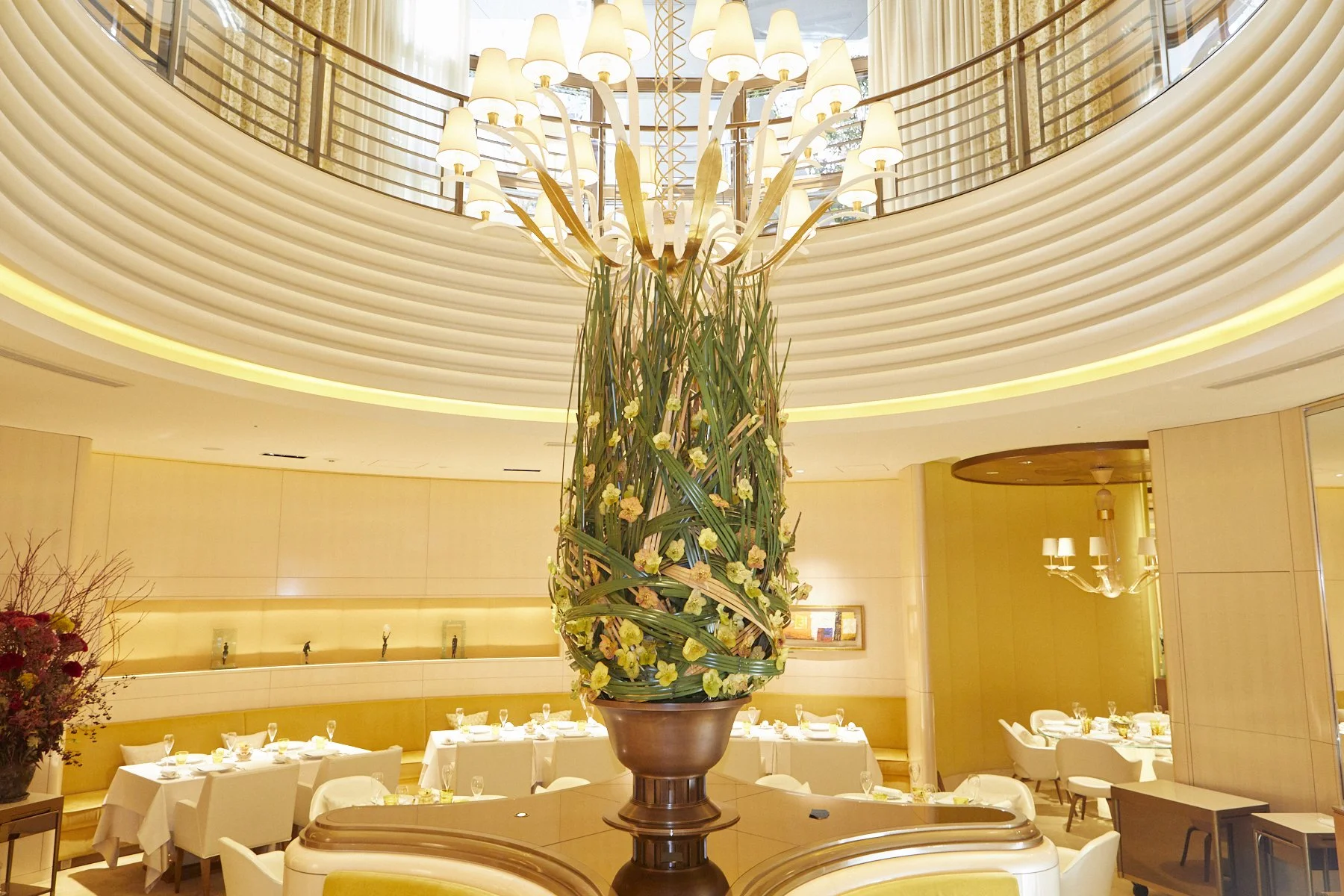 Hotel restaurant floral installation with tall sculptural arrangement of woven leaves and yellow blooms complementing modern architecture.
